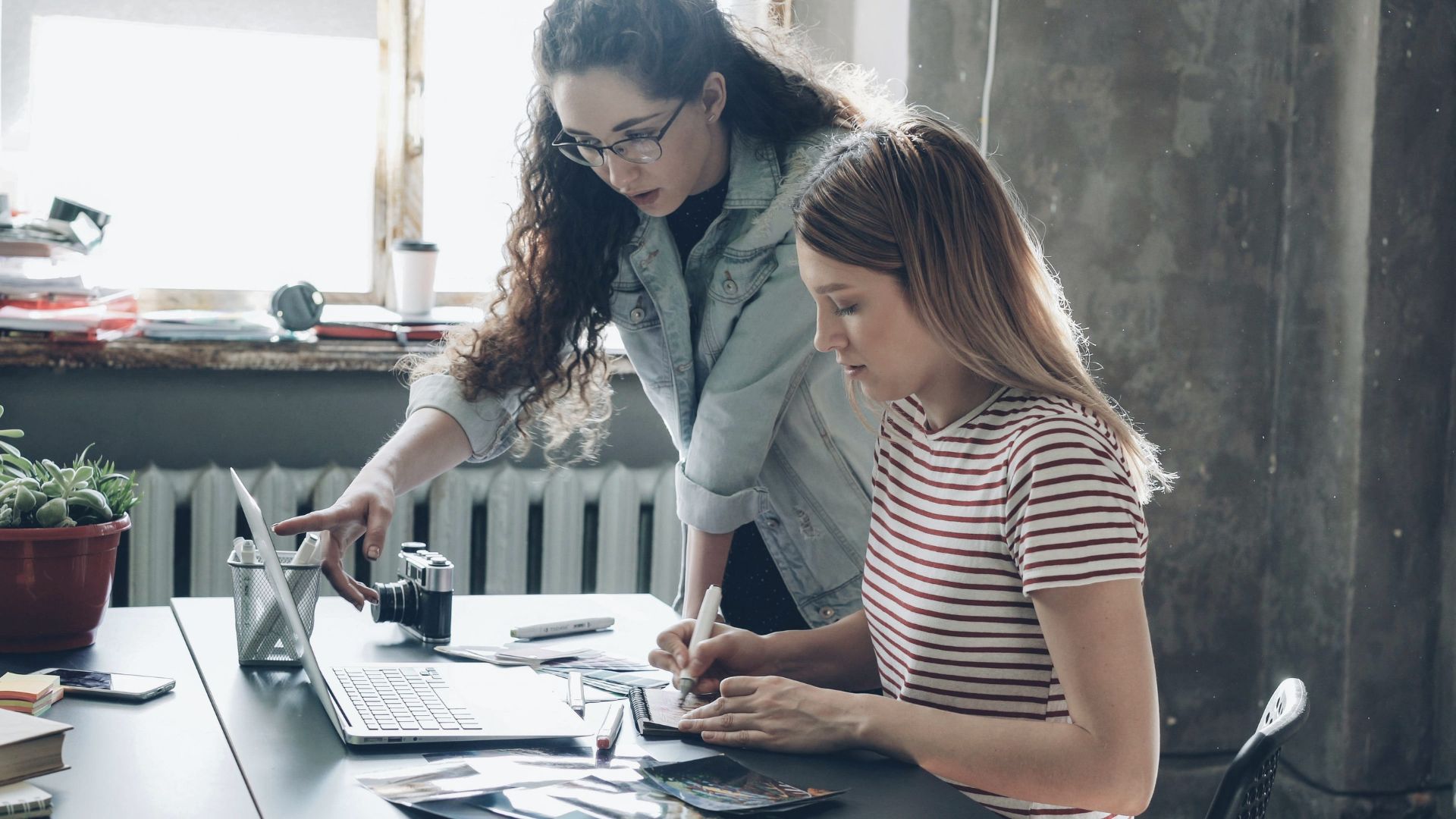 Two female designers collaborating on a creative project using a laptop and sketches