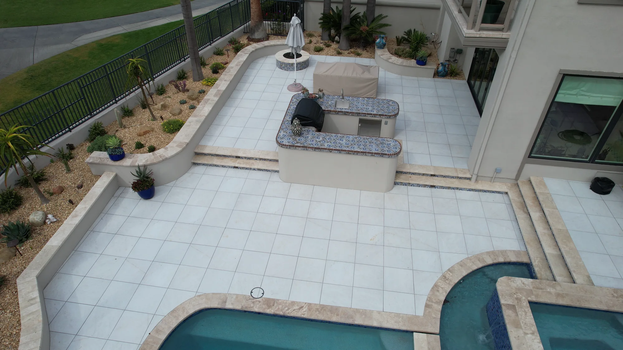 Overhead view of an outdoor kitchen island, wide paved terrace and steps beside the swimming pool.