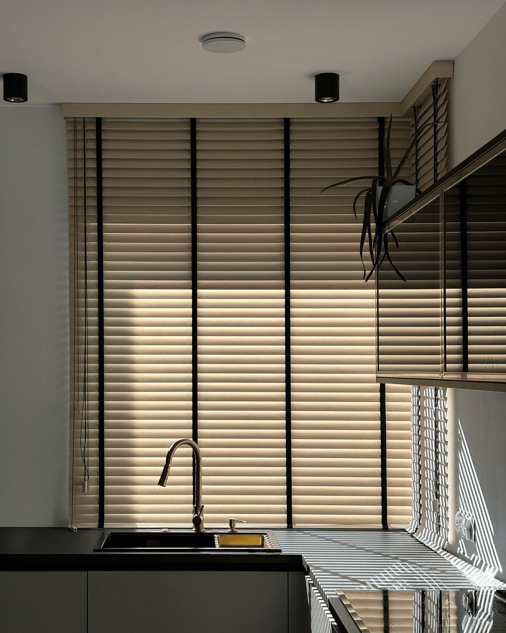 Eleganckie beżowe żaluzje drewniane z czarnymi taśmami w nowoczesnej kuchni. HeyShade Pruszków – luksusowe osłony okienne na wymiar z dbałością o detale.