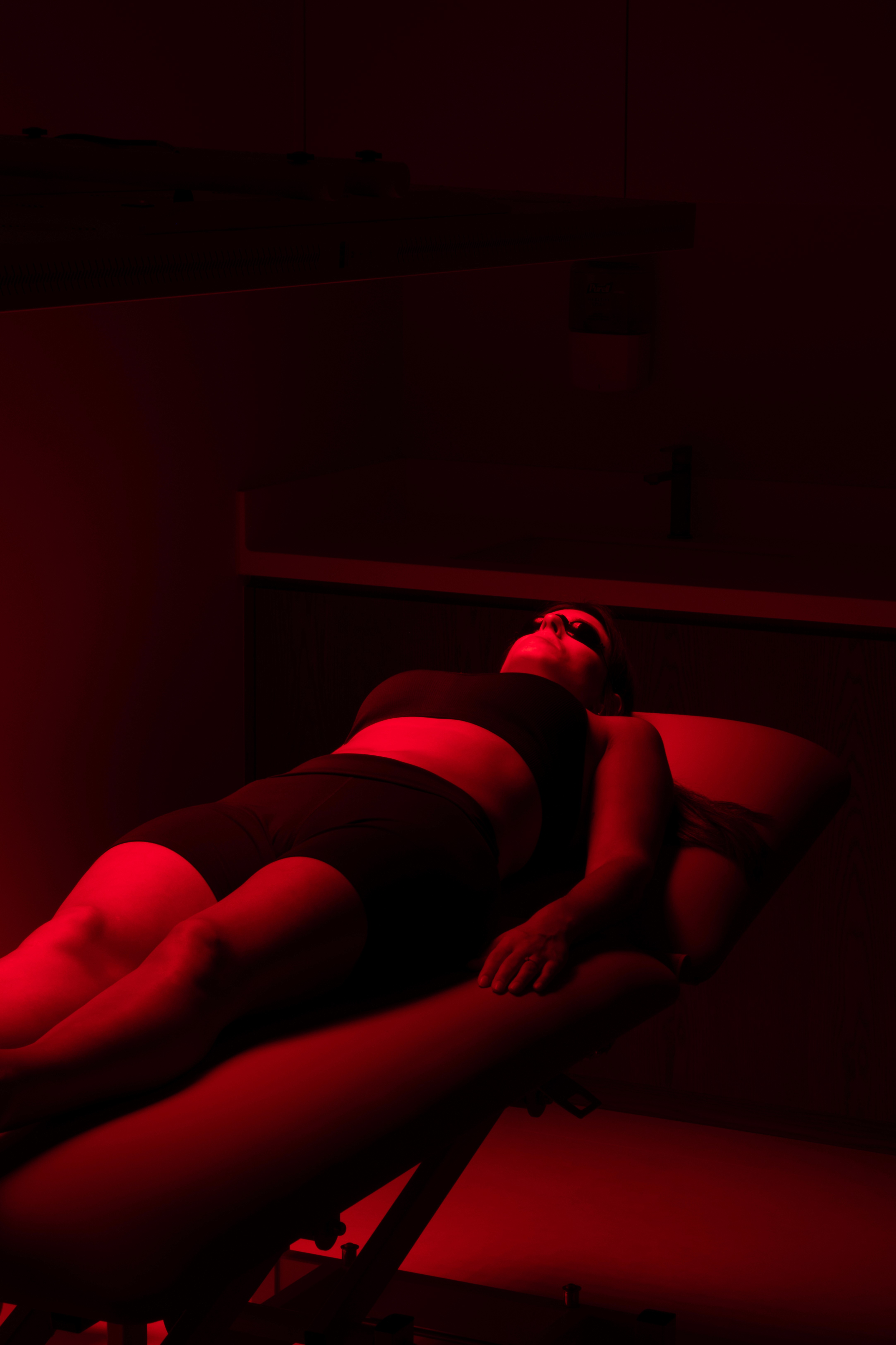 Serene treatment room with warm walnut wood paneling, a single massage table on a woven rug, floating stone shelf with apothecary bottles, and a fiber optic star ceiling