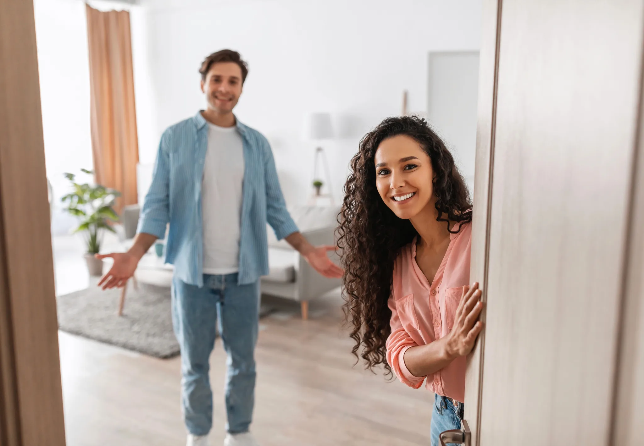 A female standing in the doorway, her husband behind her, welcoming guests in to their home.