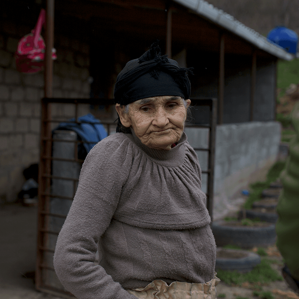 An elderly woman standing outside her home