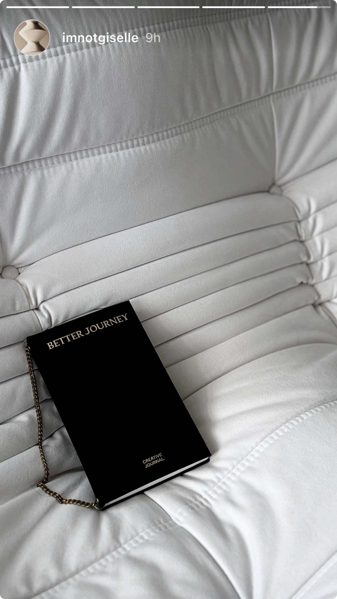 Black BETTER JOURNEY Creative Journal with brass chain bookmark, resting on white bedding, showcasing its elegant design in a cozy setting