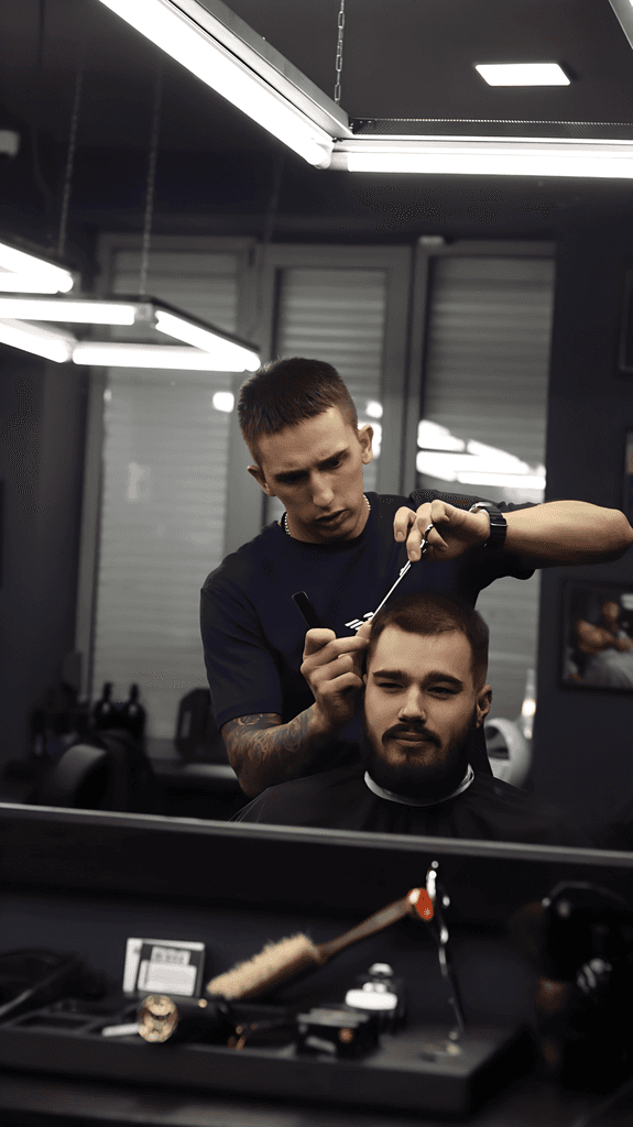 A barber trims a man's hair in a modern barbershop with sleek lighting and mirrors.
