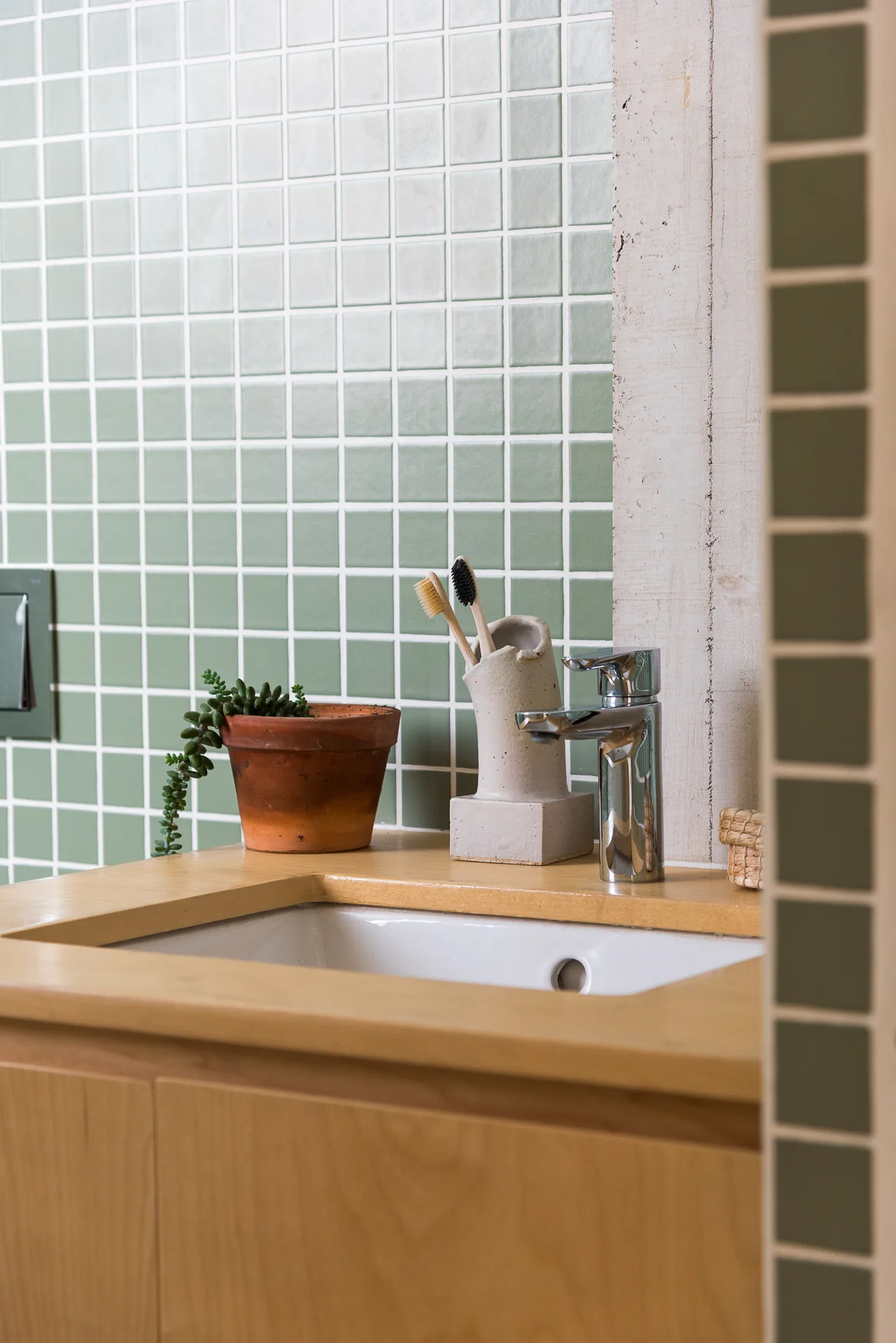 Lavabo empotrado en cubierta de madera con planta y mosaico verde