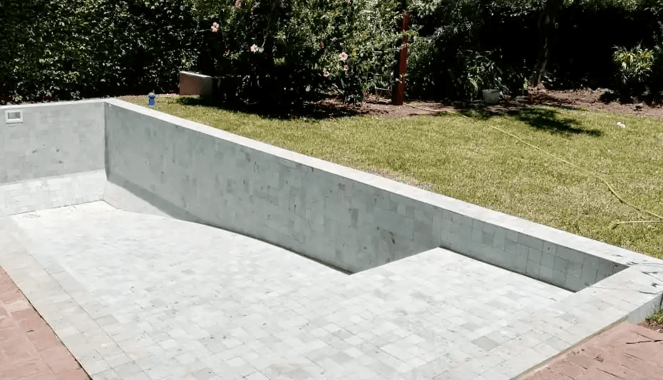 Construcción de pileta de hormigón en jardín, mostrando la colocación de revestimiento premium de Piedra Bali en tonos claros.