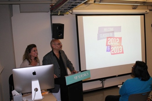 two older people are giving a presentation, and next to them is an image projected on the right side