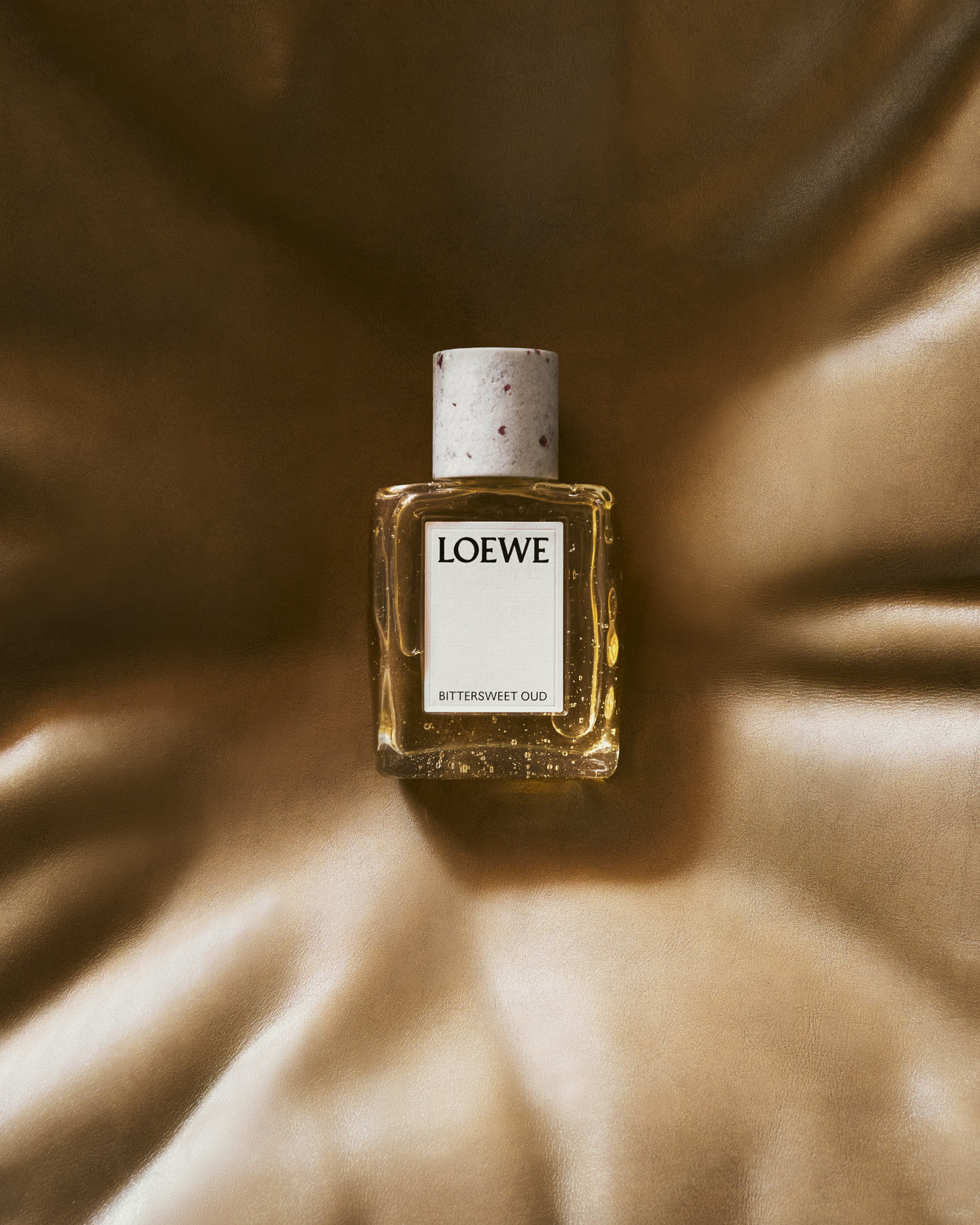 LOEWE Bittersweet Oud fragrance bottle resting on camel leather armchair.