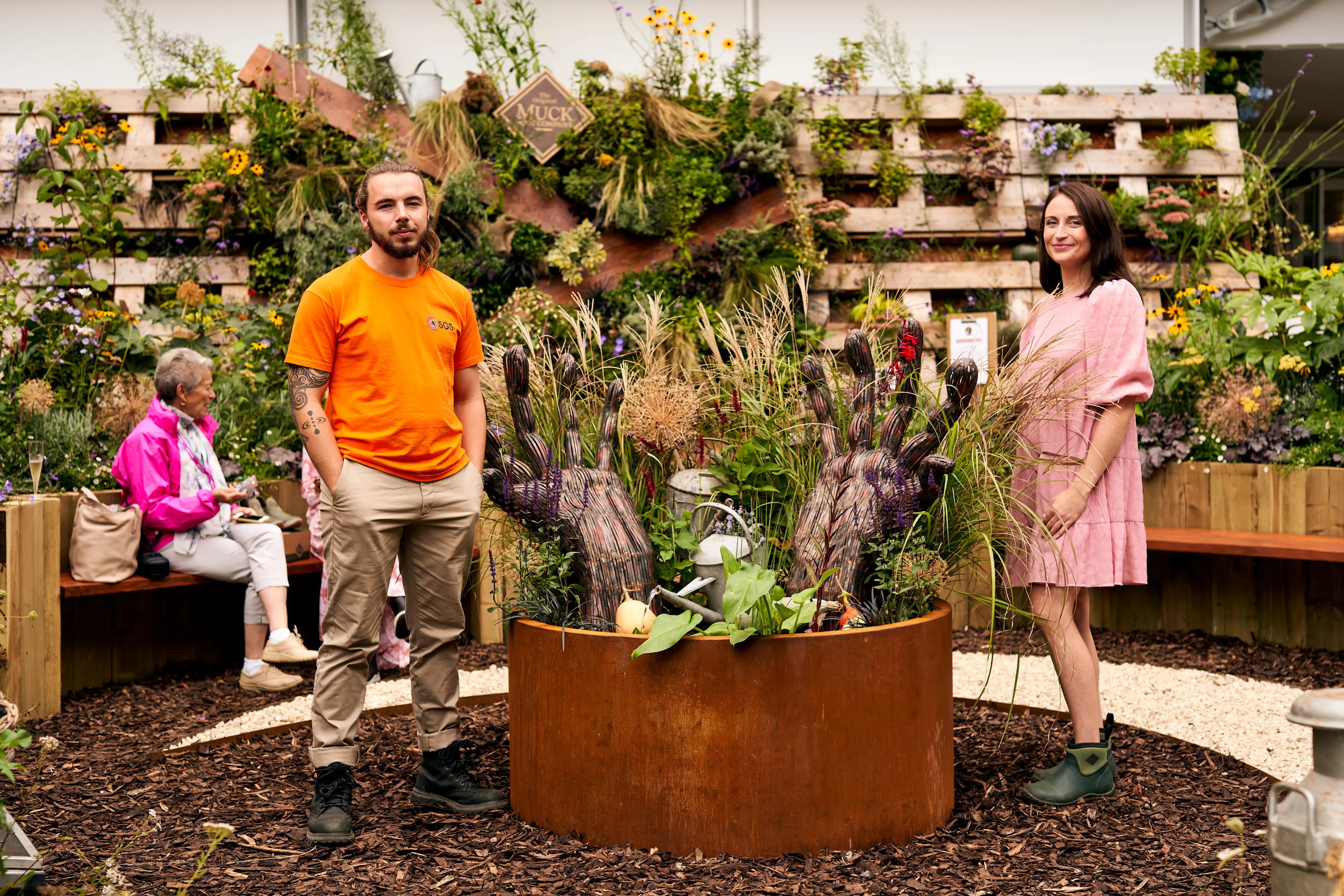Four people stand in a garden with lush plants, smiling and enjoying their time together in a sunny outdoor setting.