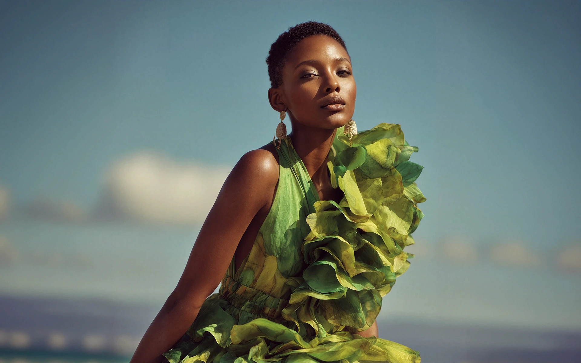 A woman in a vibrant green ruffled dress poses confidently against a clear blue sky, showcasing elegance and style.