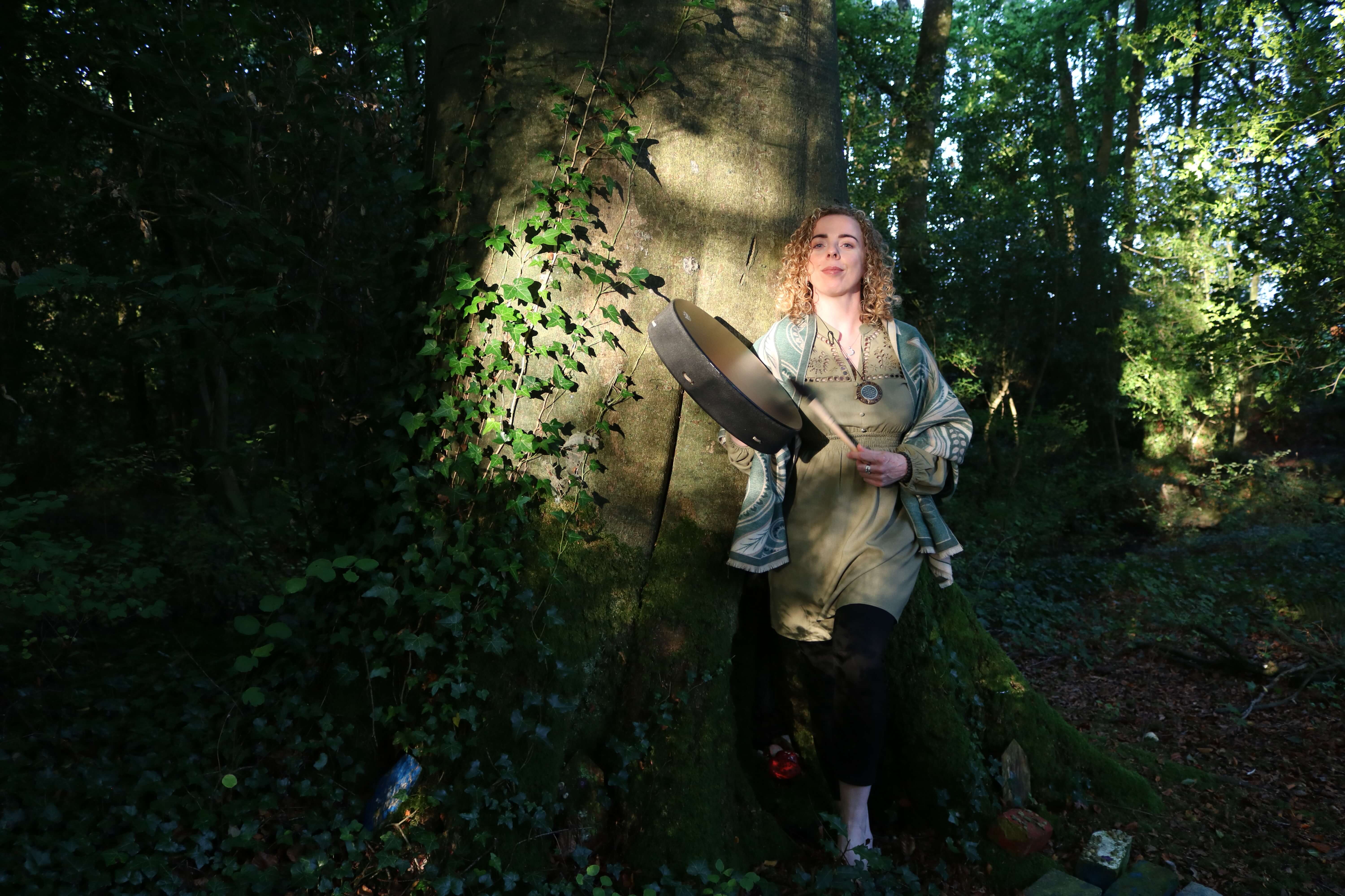 Maryrose standing up against tree playing the drum