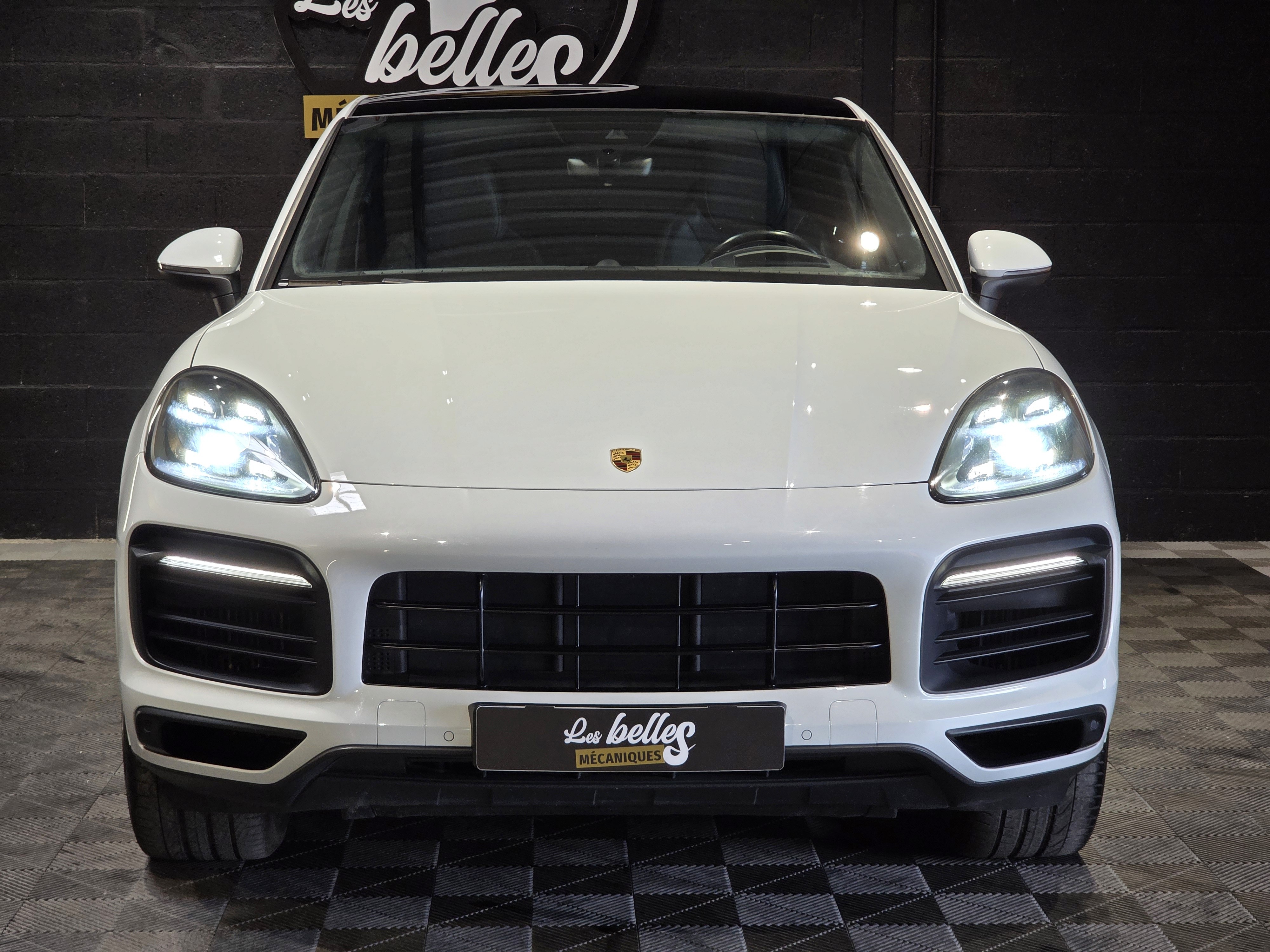 Face avant du Porsche Cayenne Coupé blanc carrara avec phares LED Matrix allumés, badge Porsche central, Les Belles Mécaniques