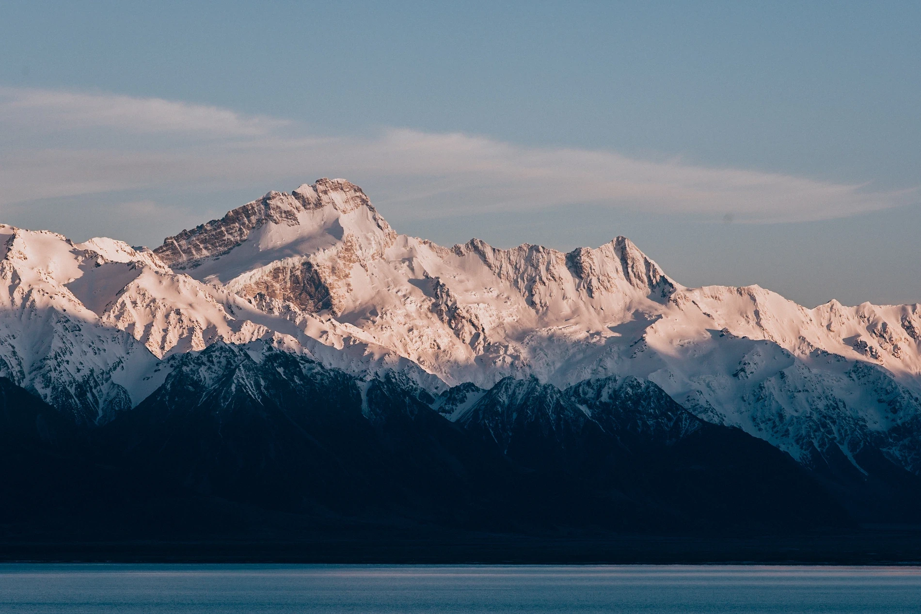 A long snow-covered mountain range lit soft above a dark lake