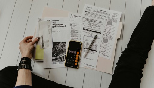 A hand holding magazines and papers with a smartphone on a wooden surface.