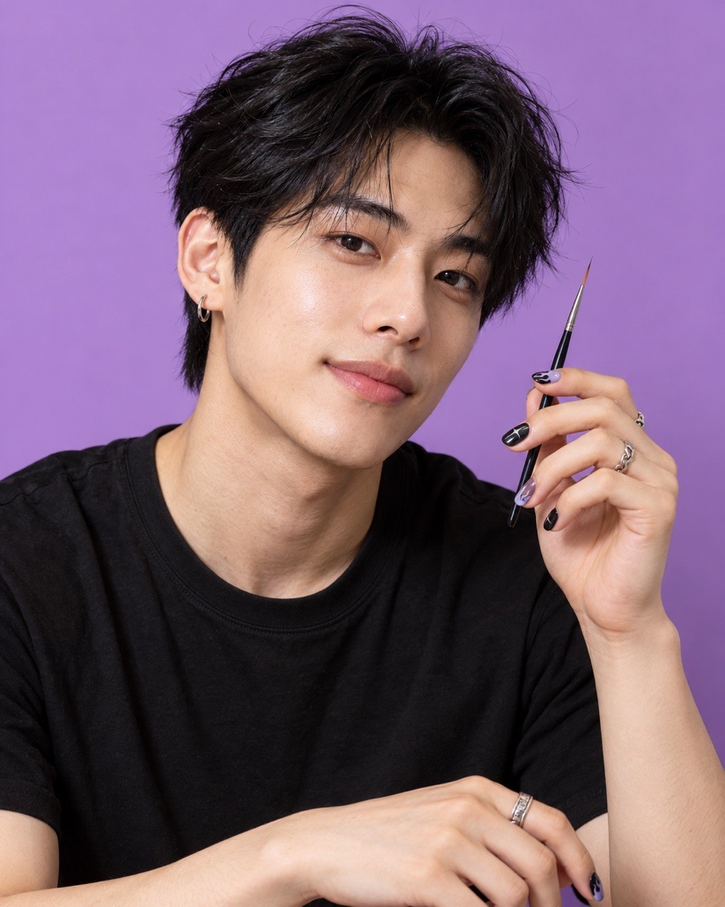 Jun, a nail artist in a black t-shirt holding a nail art brush on a lilac set.