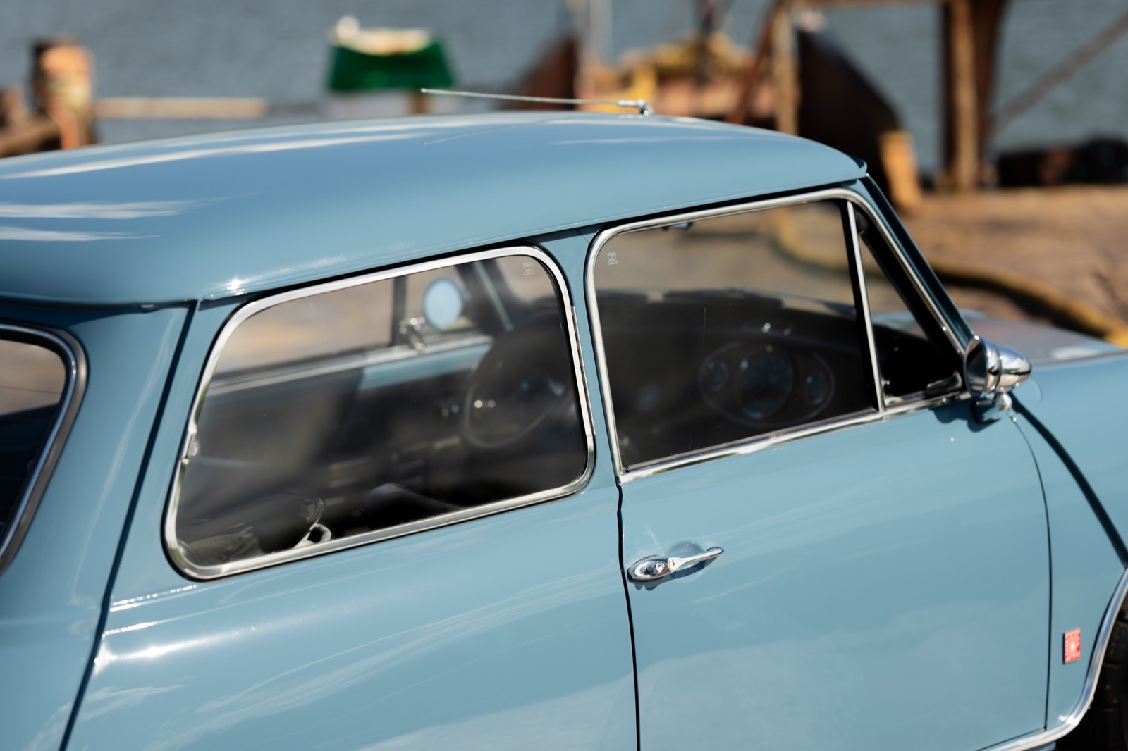 Close-up of a vintage blue car's window and roof under bright sunlight, with a blurred background.