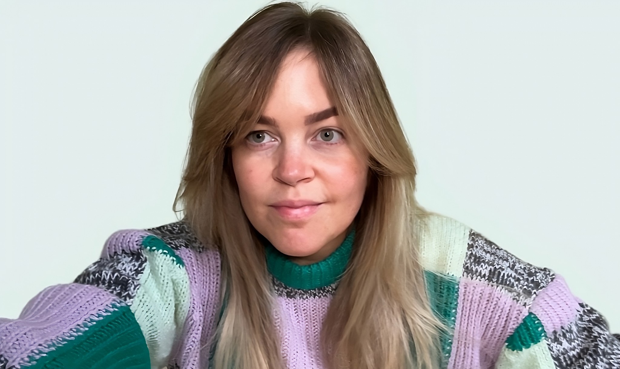 Woman looking away from the camera that is wearing a dark and light green, purple, and grey sweater.