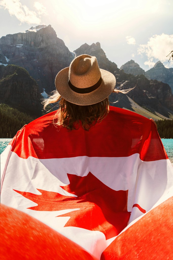 A new Canadian citizen wrapped in a Canadian flag, looking at the Rocky Mountains, ready to travel with her first passport.