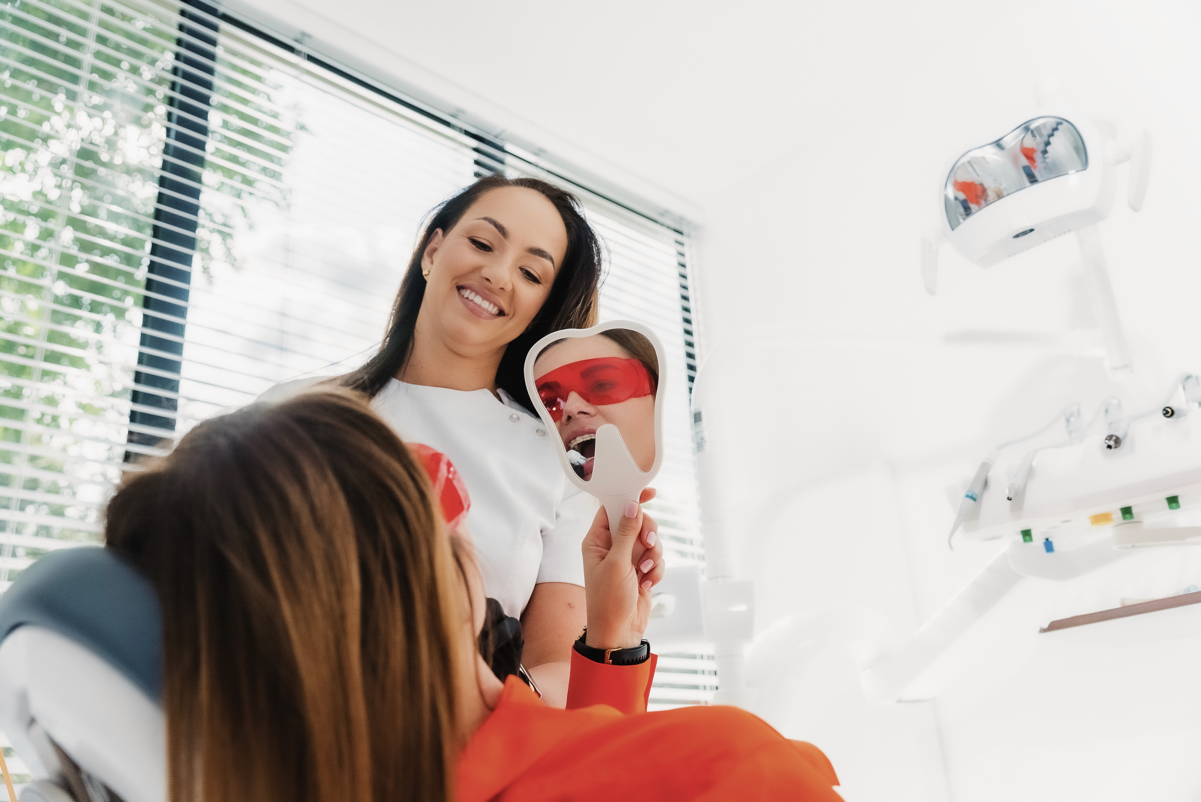 Dentystka z pacjentką na fotelu stomatologicznym, pacjentka ogląda zęby w lusterku.