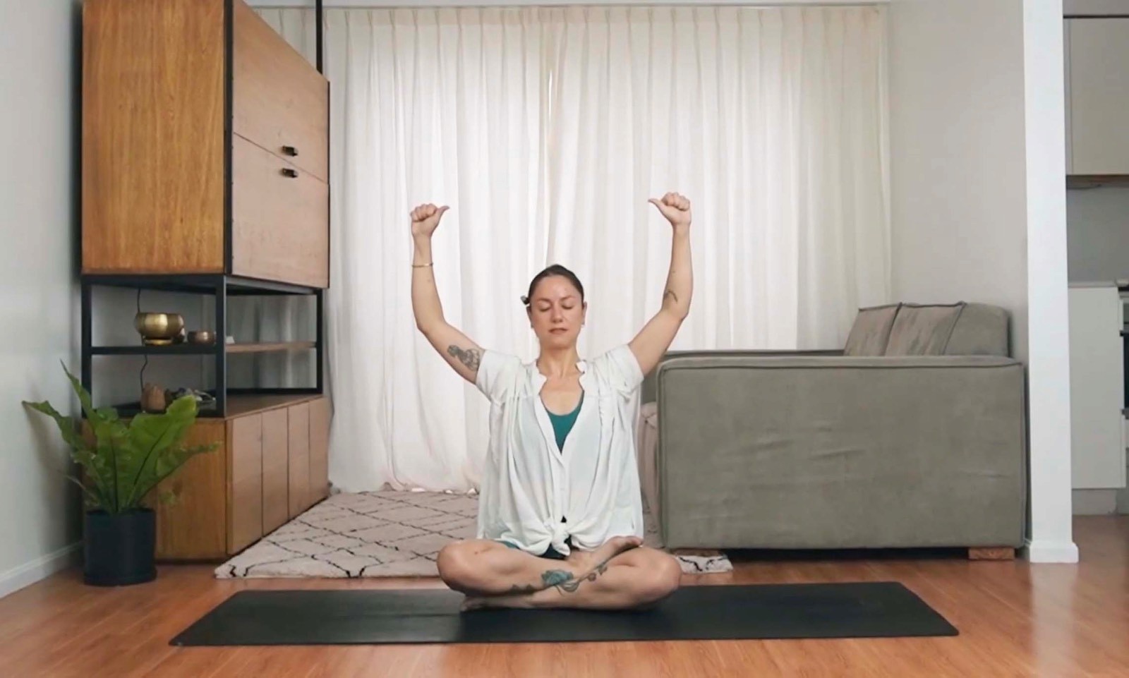 Flavia Siutti sentada en una esterilla levantando los brazos al iniciar una práctica de yoga.