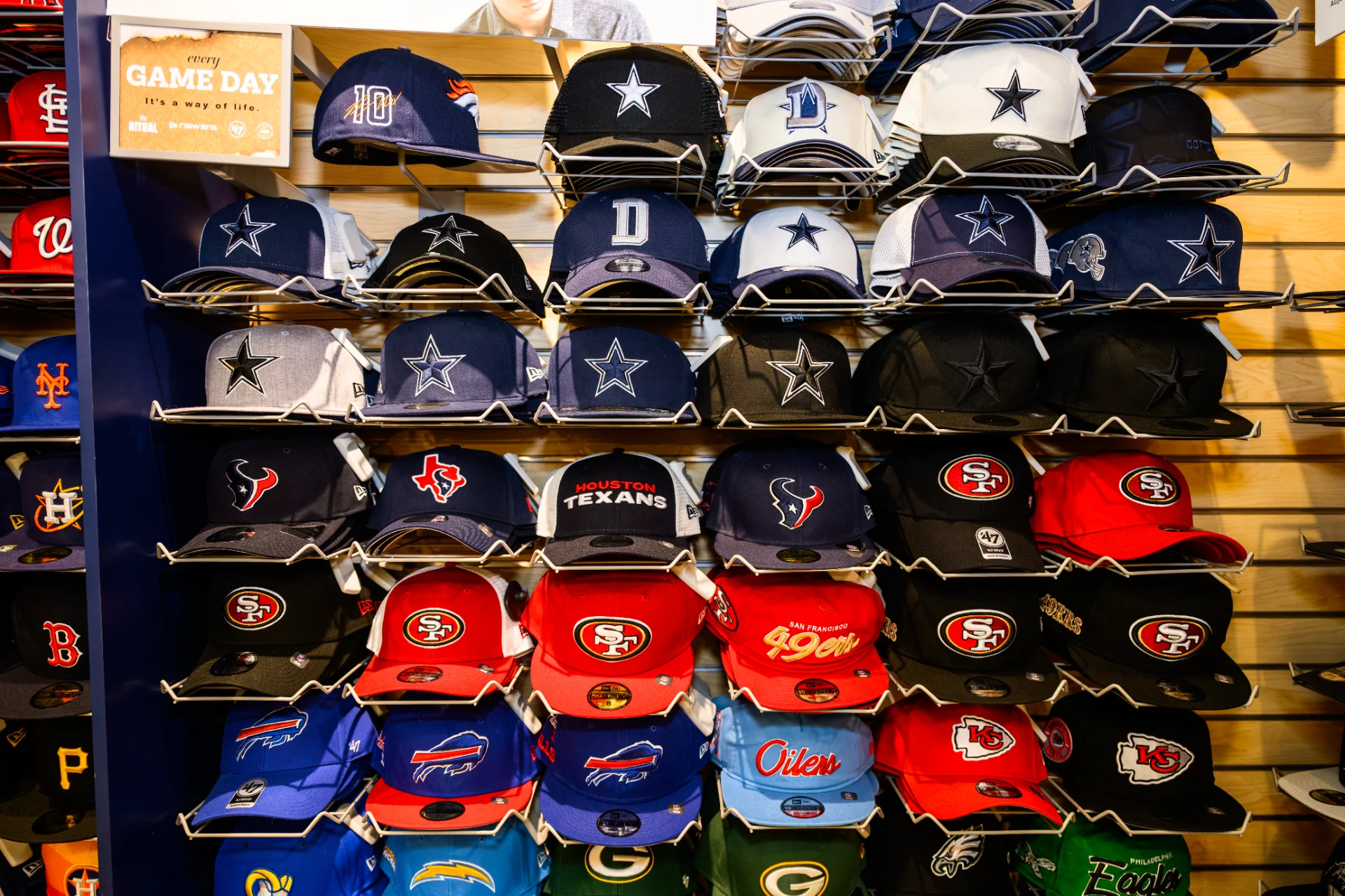 Wall display of MLB and NFL fitted caps at Lids, including Cowboys, Texans, and 49ers designs