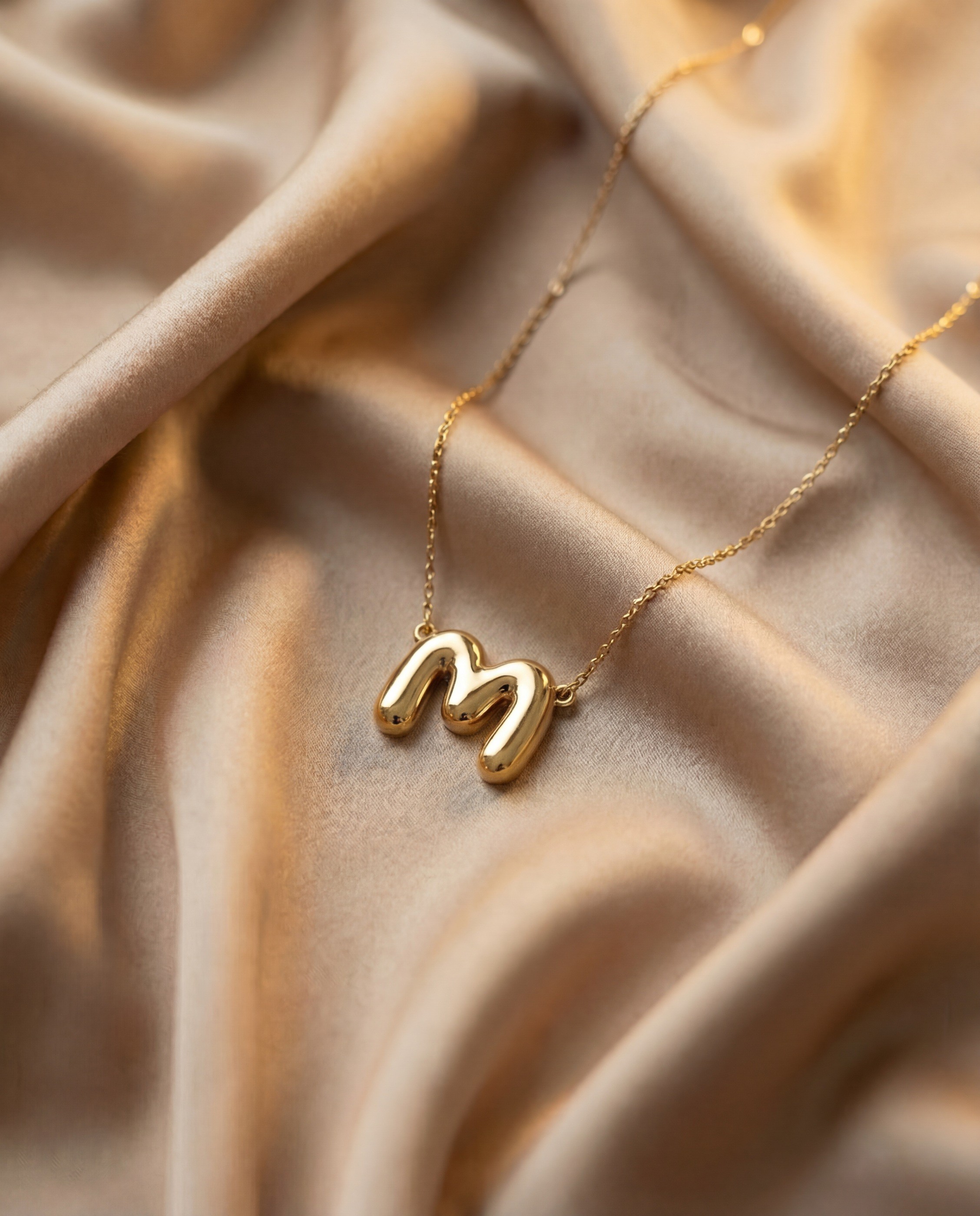 Vedder & Vedder — Gold initial M pendant on softly folded satin.