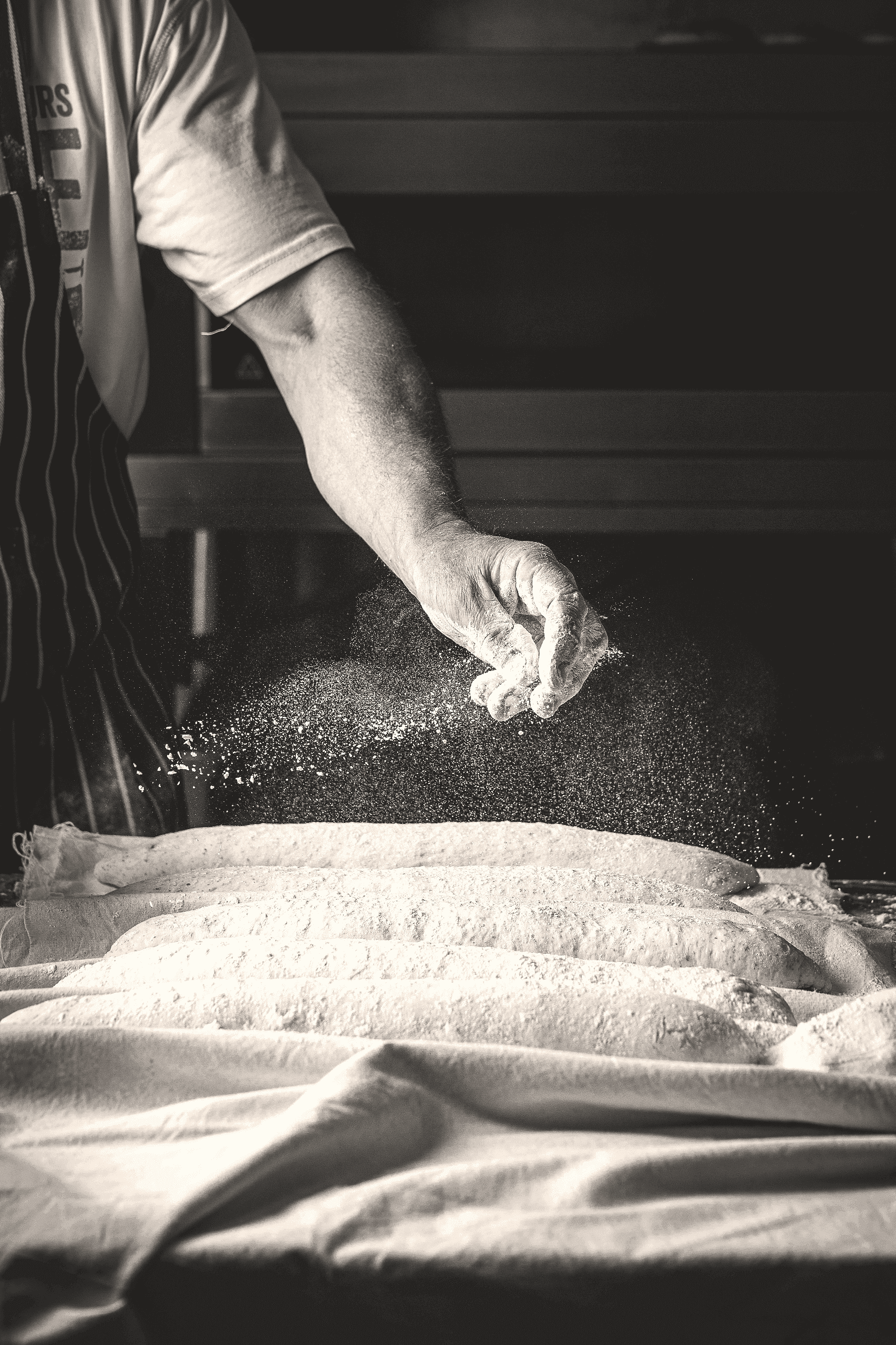 A person in an apron sprinkling flour on a table