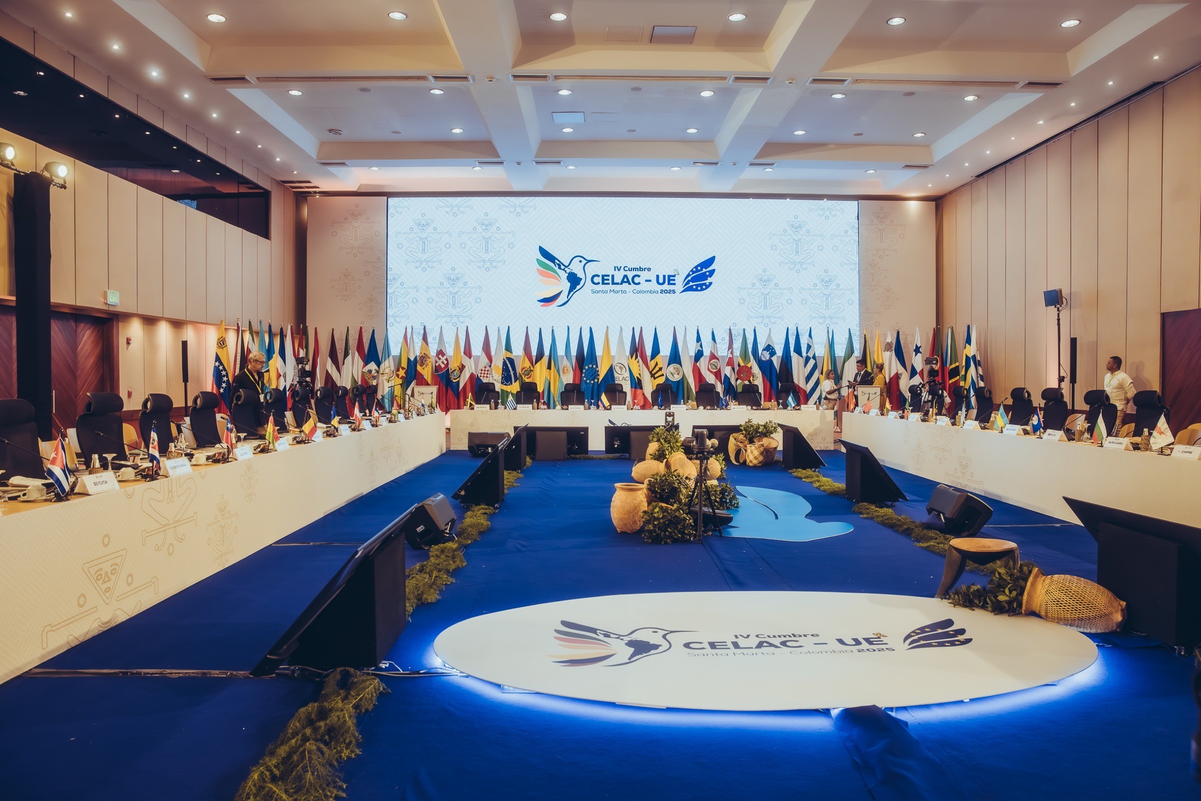 Salón plenario de la IV Cumbre CELAC-UE con la mesa en herradura, las banderas y el logo del evento en el piso