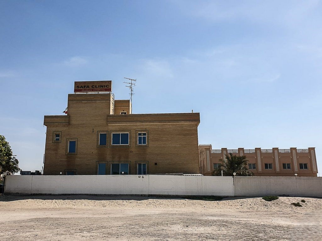 The two-story, light brown brick building of the Safa Clinic, featuring its red and white sign on the roof, against a blue sky.