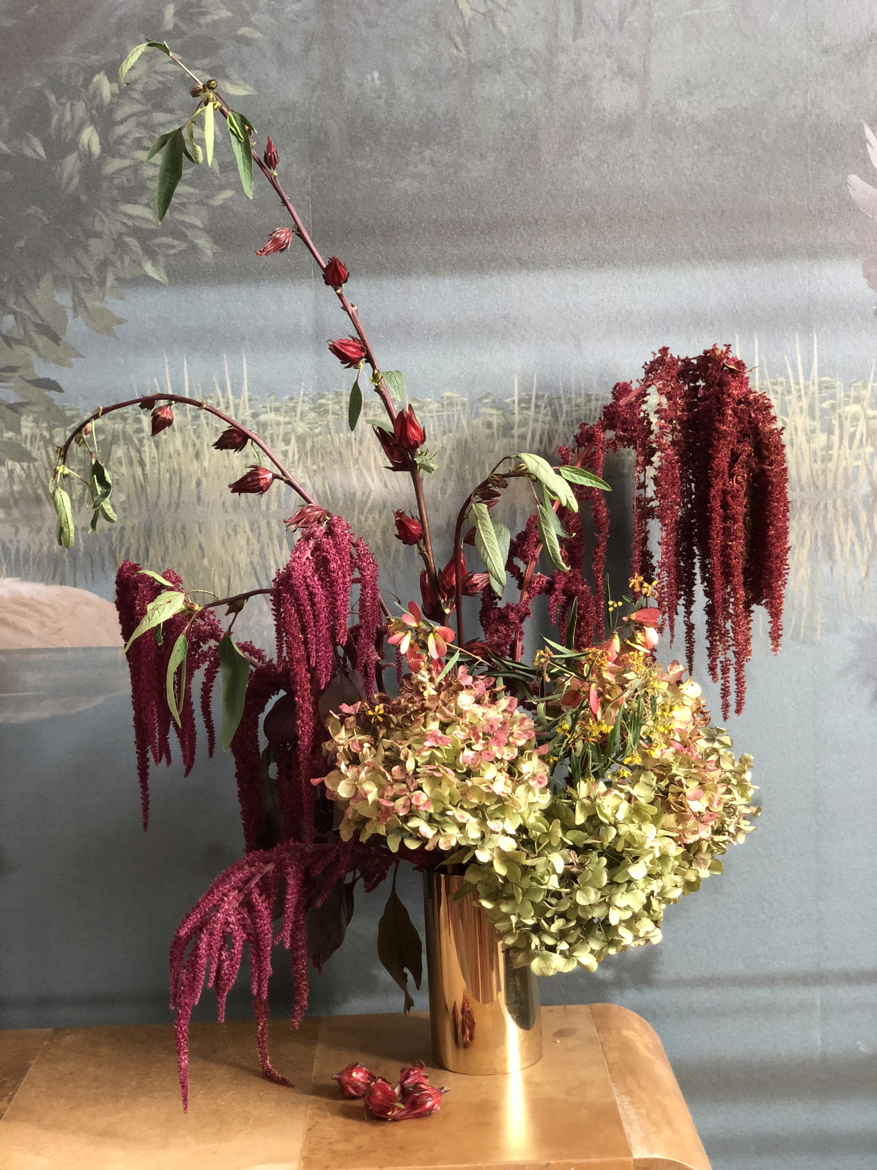 Arreglo floral con hortensias y amaranto rojo en jarrón dorado, composición elegante de estética natural y sofisticada.