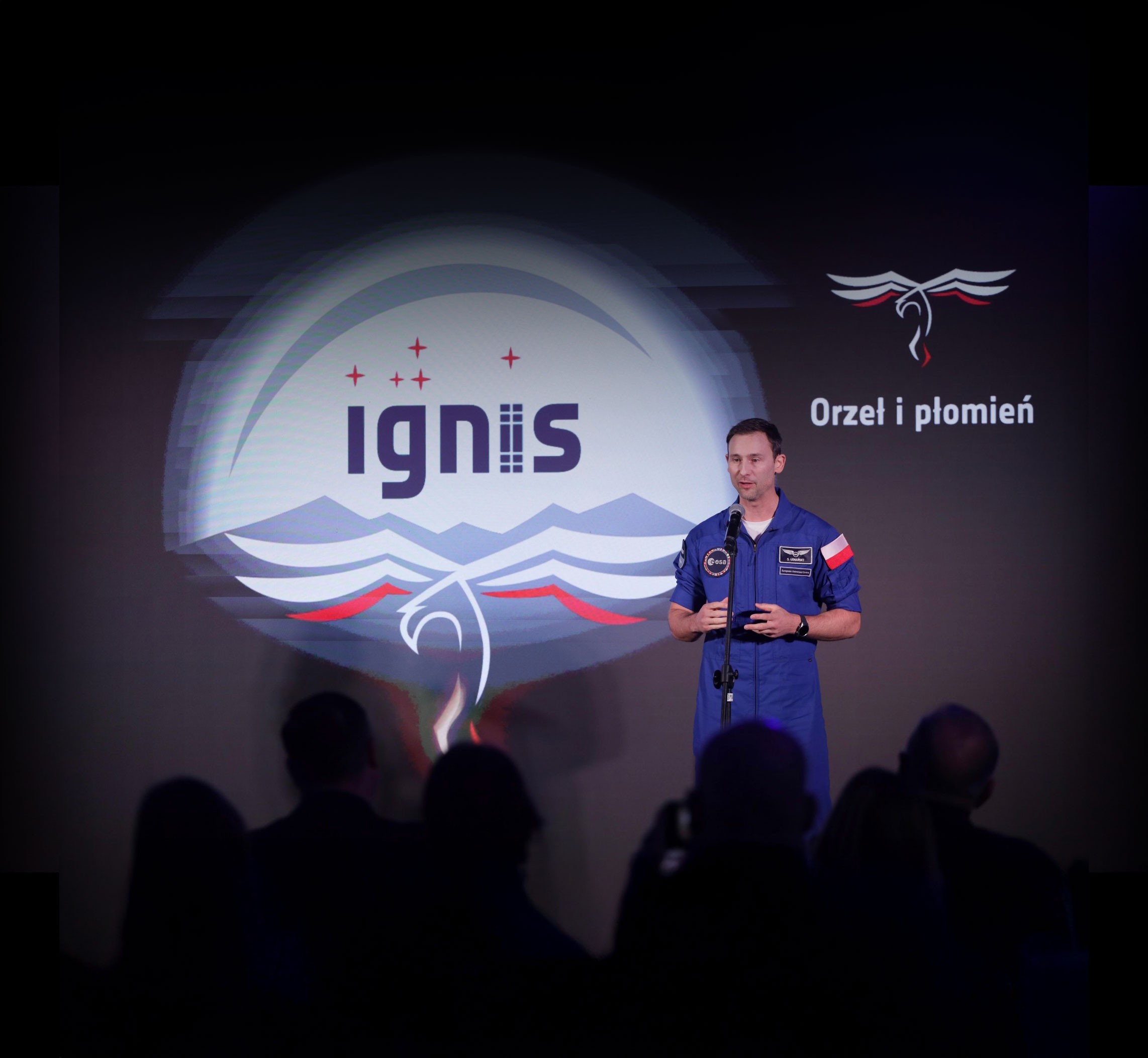 Sławosz Uznański prezentuje misję kosmiczną IGNIS – Orzeł i płomień, w kombinezonie ESA i z flagą Polski