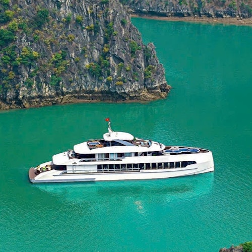 En elegant hvid yacht flyder på turkisblåt vand nær klippefyldte, træklædte klipper.