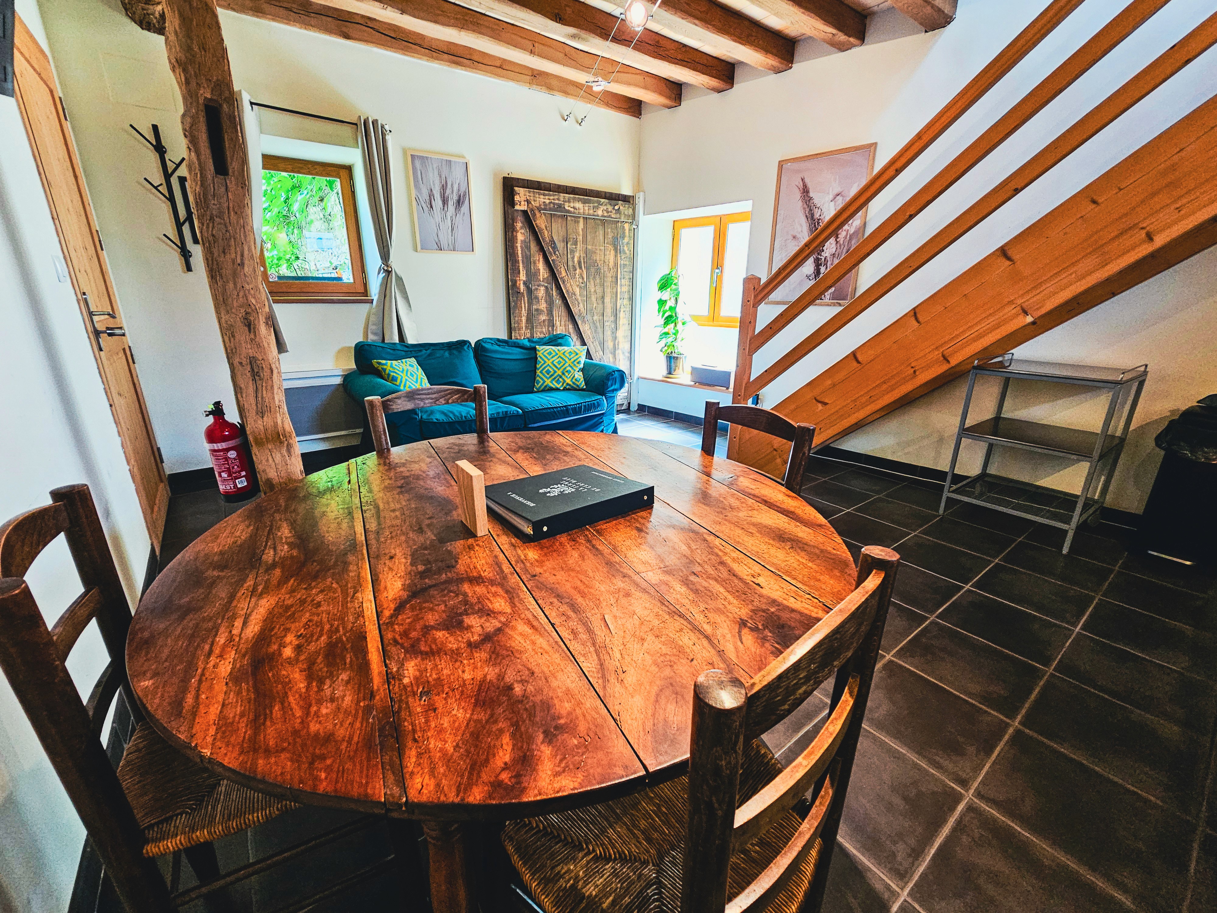 Salon avec table en bois, canapé et escalier apparent.