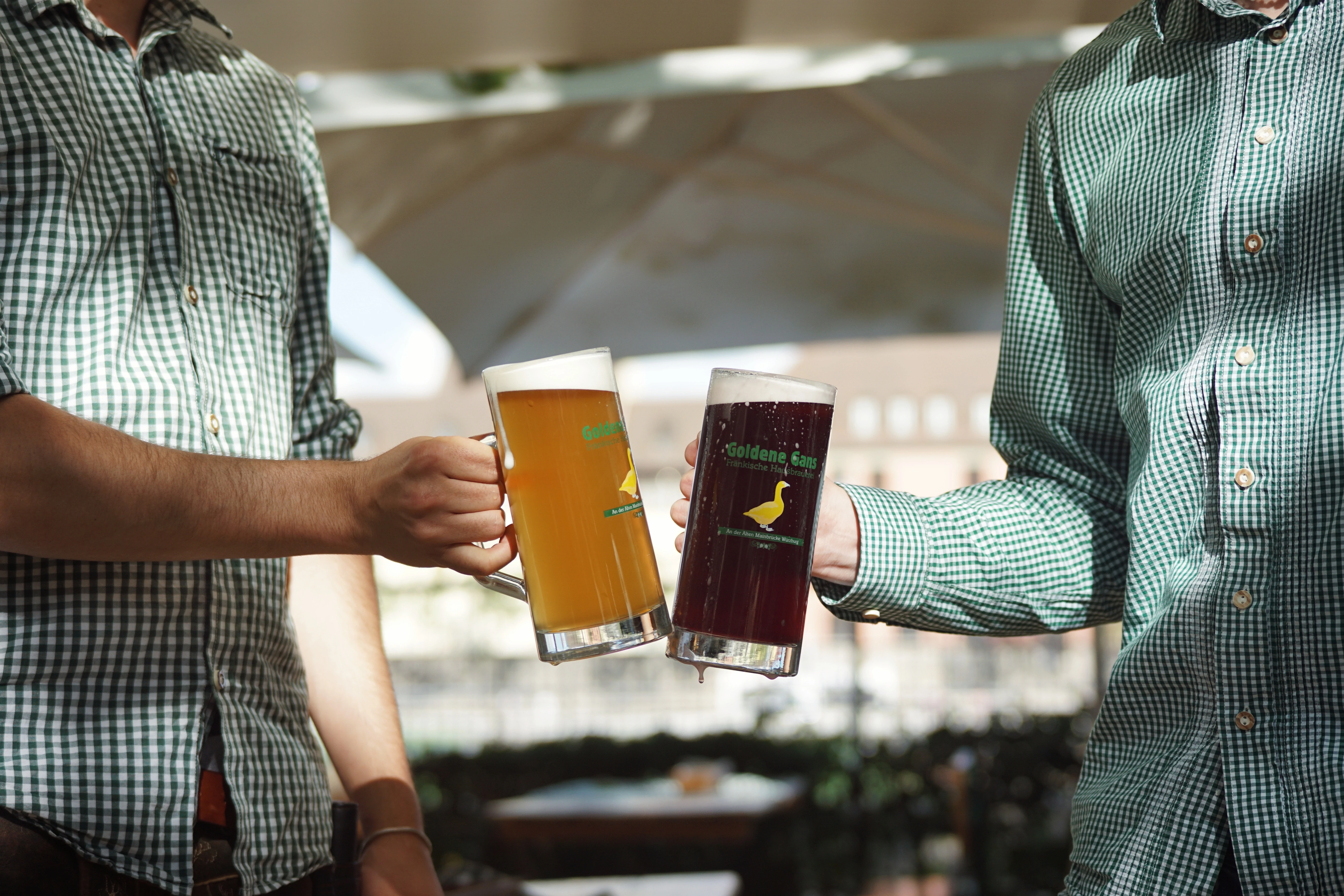 Zwei Personen stoßen mit großen Bierkrügen, helles und dunkles Bier, an. "Goldene Gans" Logo auf den Krügen