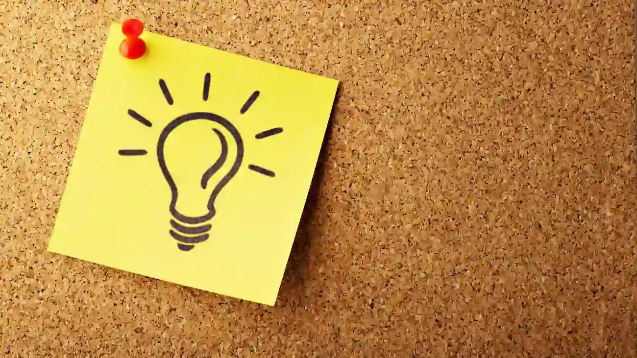 Yellow sticky note with a hand-drawn light bulb pinned to a cork board, representing sponsorship concept planning, strategy development and new partnership ideas for sports clubs.