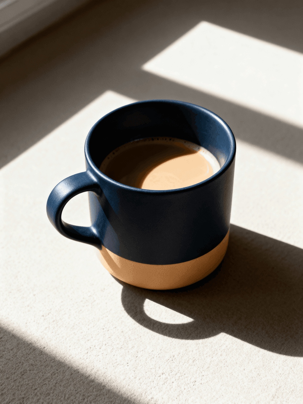 Caneca azul marinho com café sobre superfície bege com luz natural e sombras marcadas, representando o primeiro contato para contratação de consultoria estratégica.