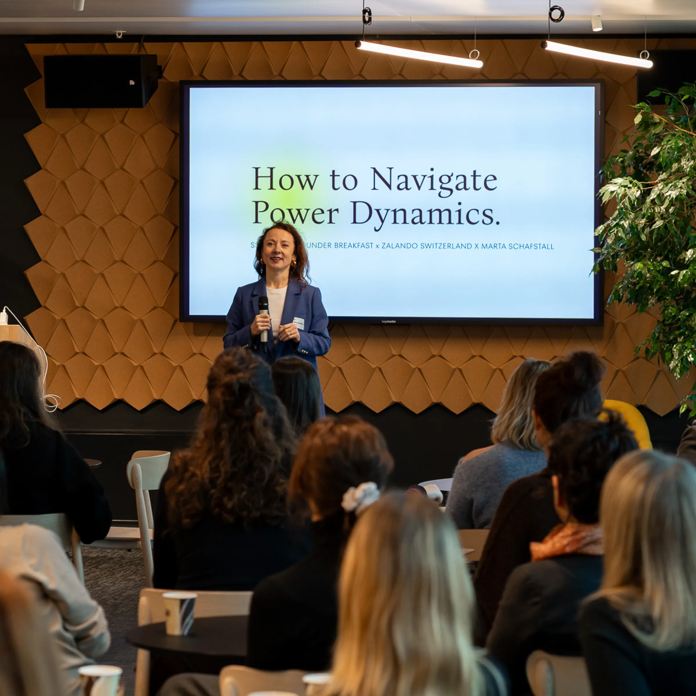 Man in a sweater smiling with arms crossed while standing by a wooden wall.