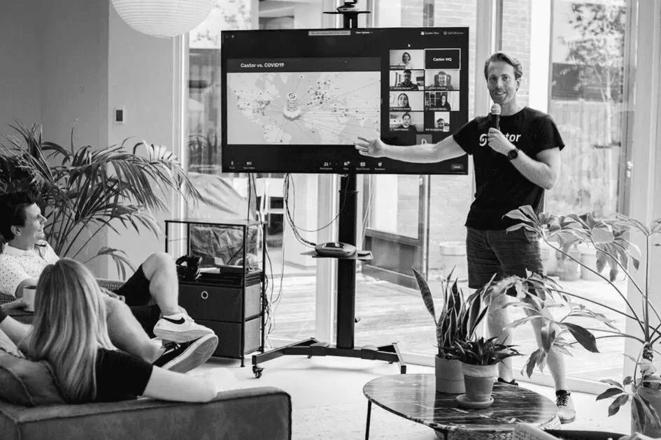 A black and white photo of a man giving a presentation using a large screen while an audience watches.