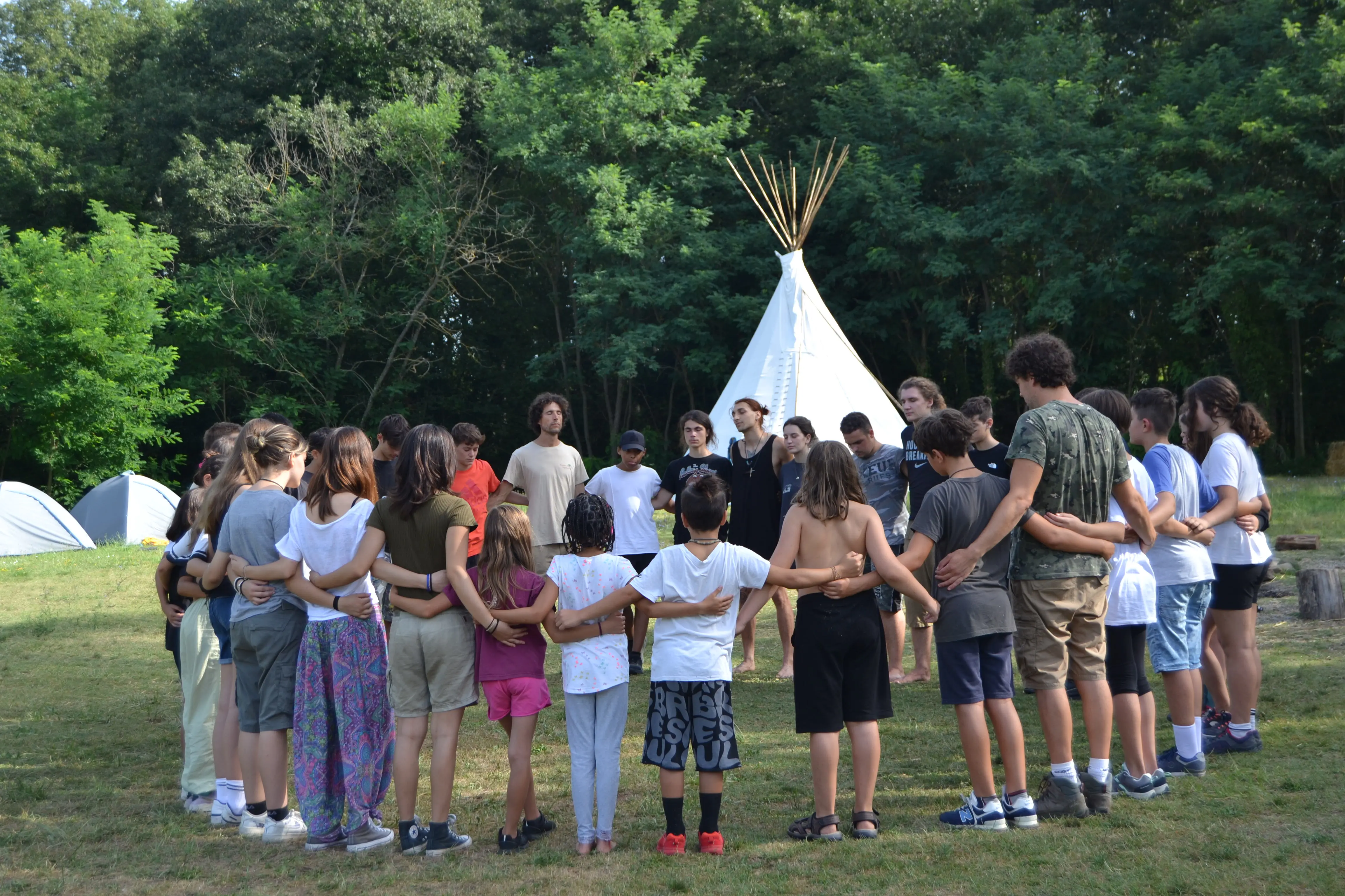 Gruppo di ragazzi in cerchio durante attività di team building in campo avventura estivo con tende e tipi, campi estivi per ragazzi 14-17 anni e percorso di crescita personale