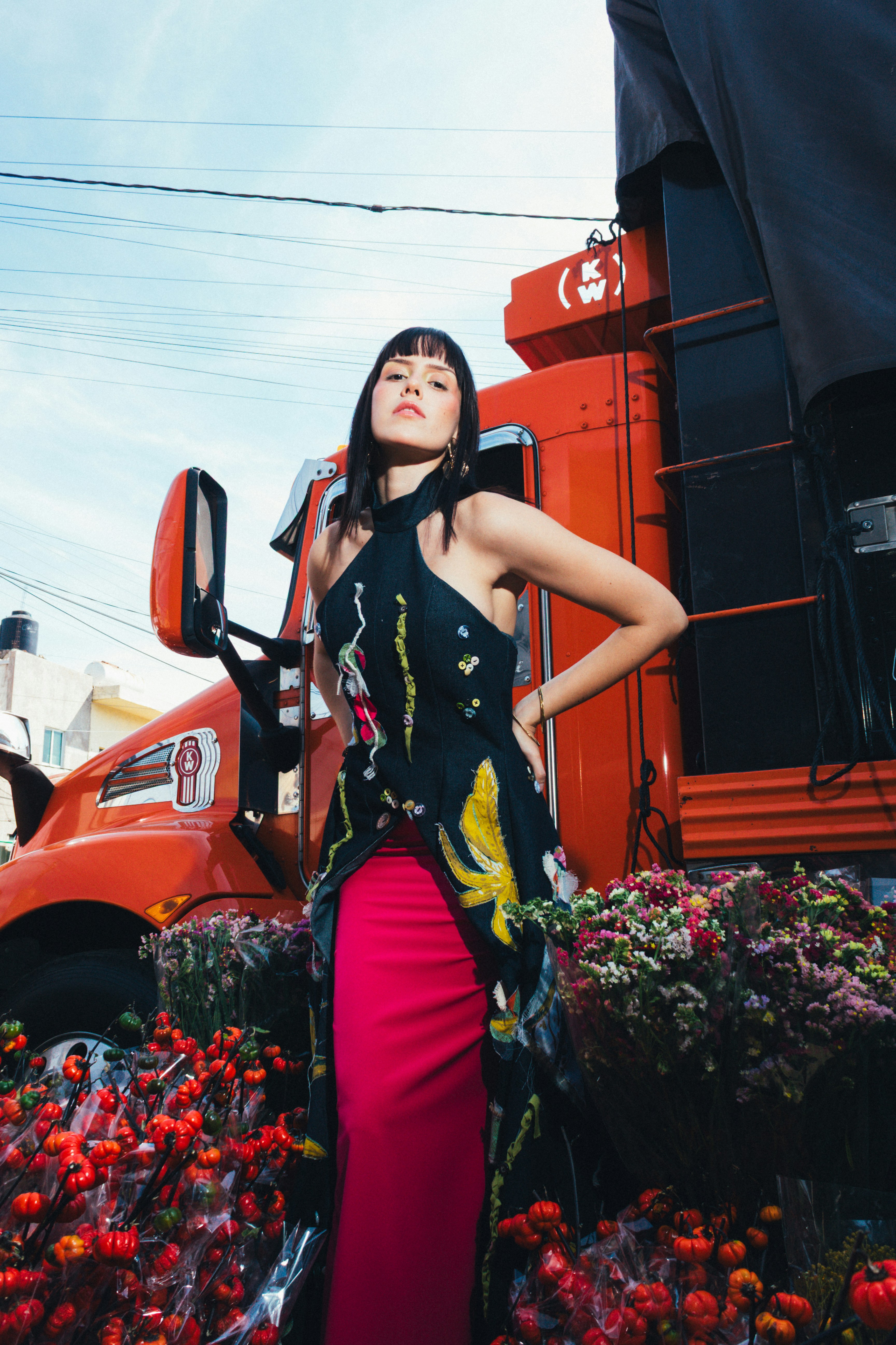 Woman in floral dress stands near orange truck and flowers