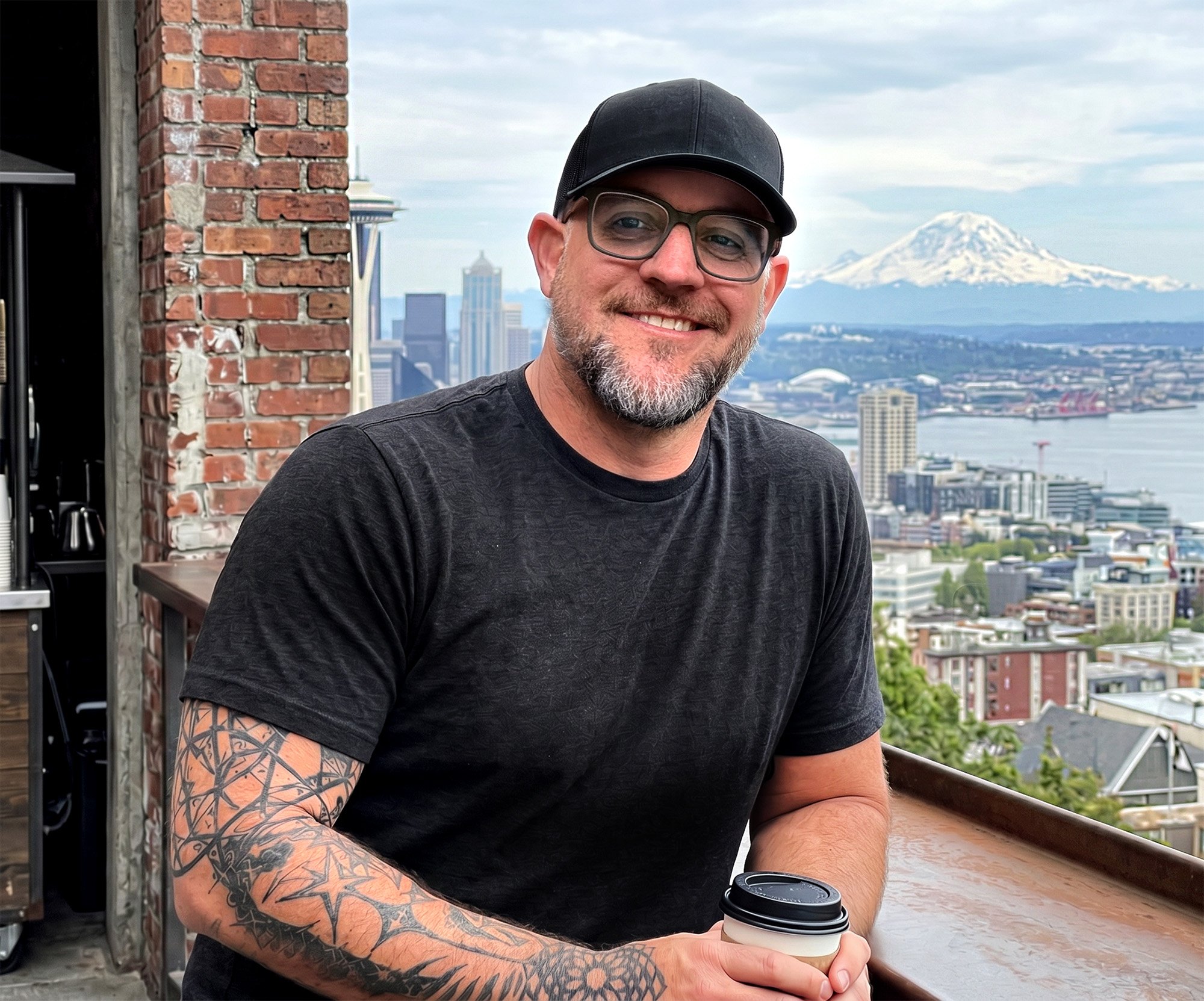 Tom Bristol smiling on a balcony overlooking the Seattle skyline with Mount Rainier in the background