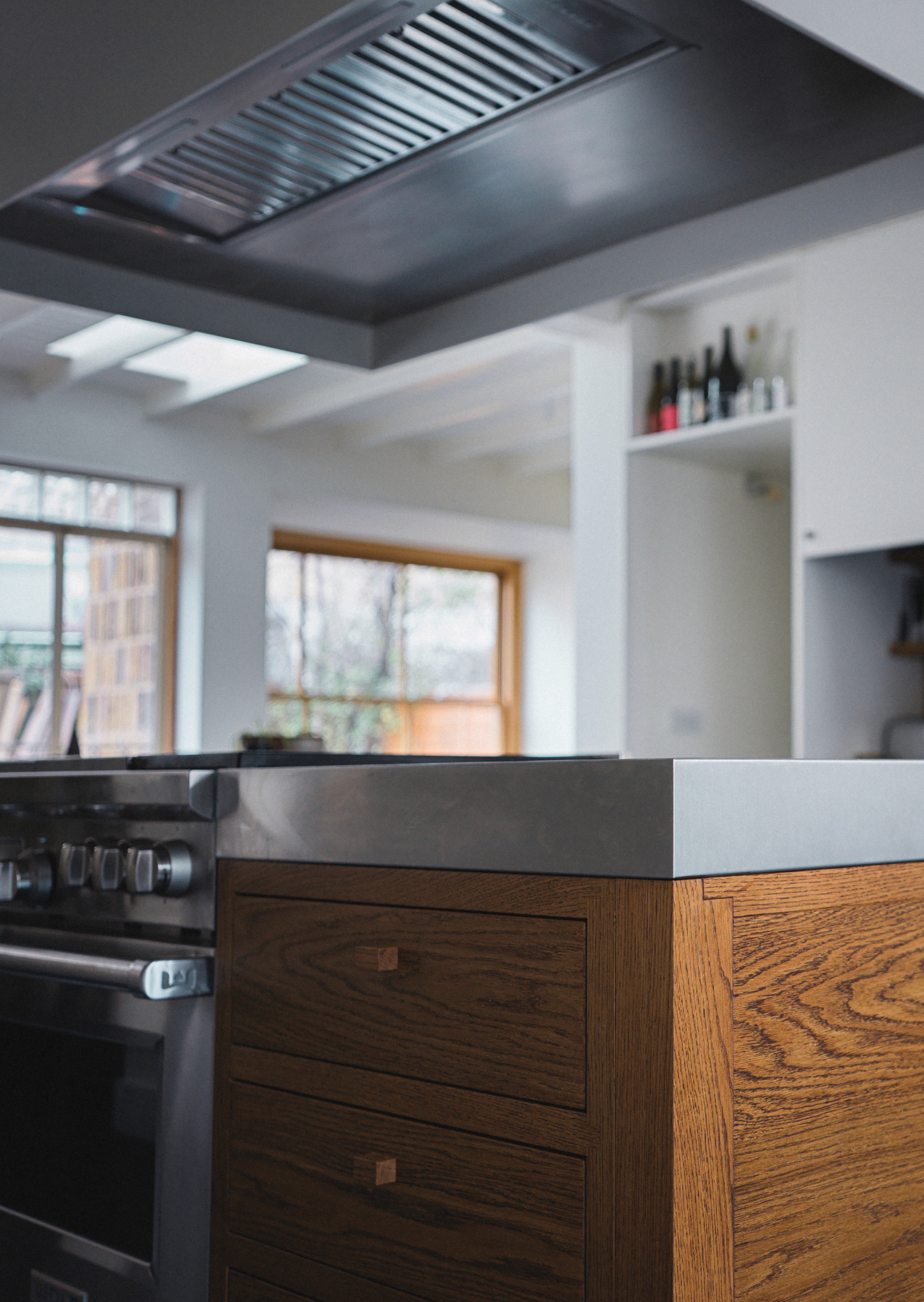 Oak kitchen island beneath large westin stainless steel extractor with natural daylight