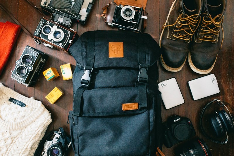 A backpack surrounded by cameras, film rolls, boots and personal effects on a dark wooden floor