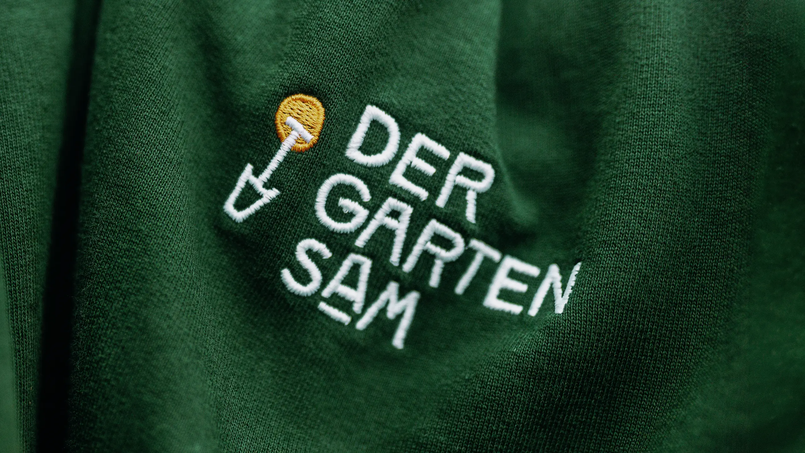 Logo „Der Garten Sam“ in Creme auf dunkelgrünem Grund