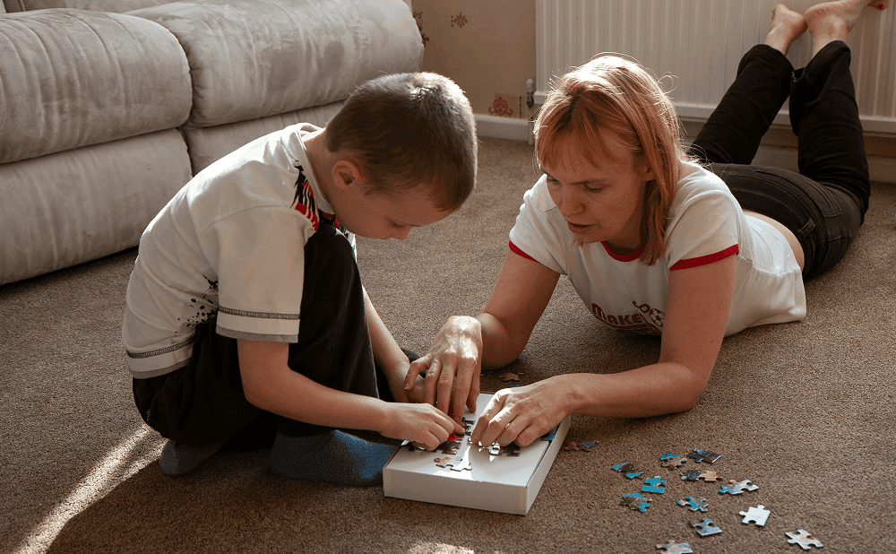 Young boy playing with puzzle pieces alongside an adult during a therapy or learning activity.