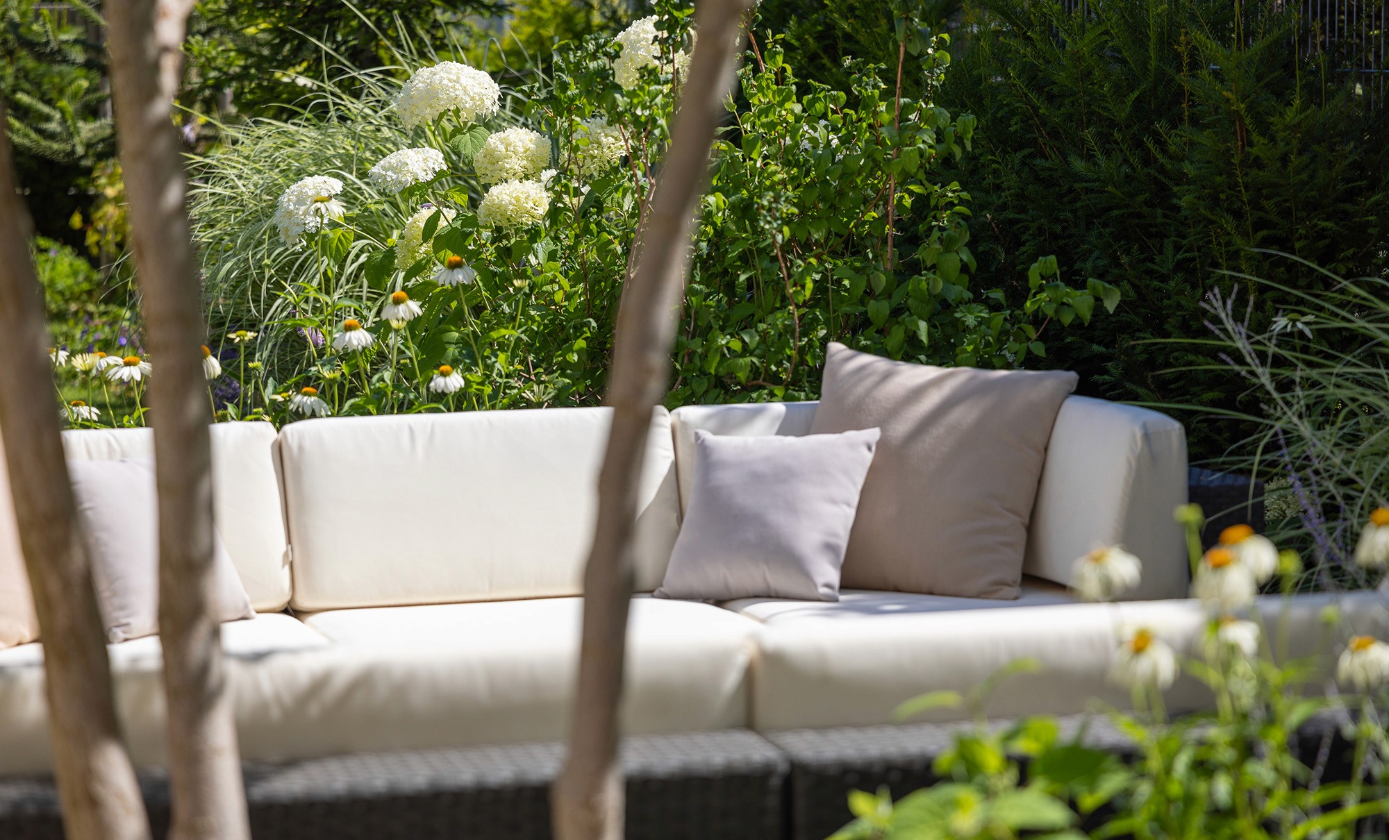 Moderner Sitzbereich mit Lounge-Sofa in naturnah gestaltetem Garten mit Hortensien, Gräsern und Stauden.