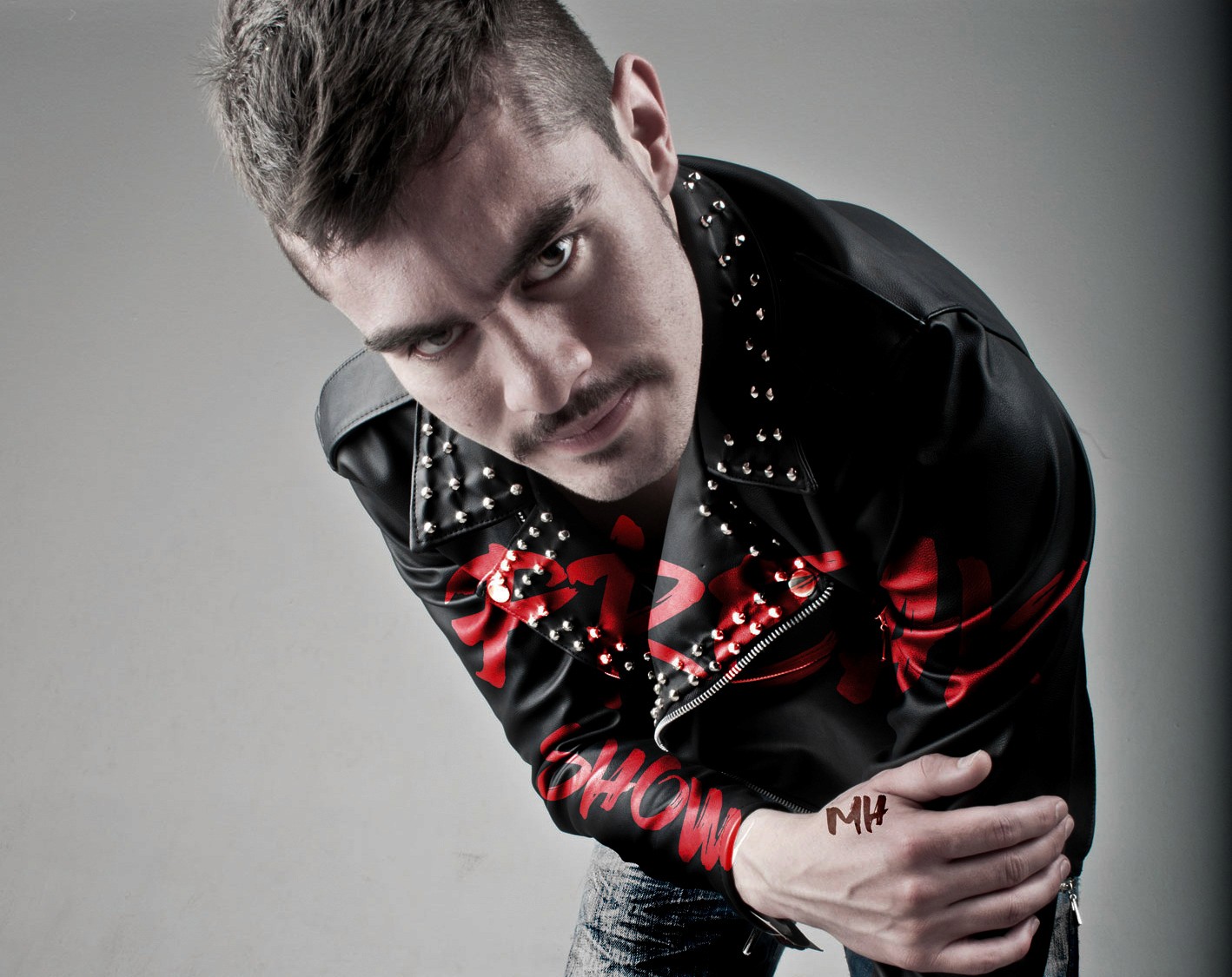 Low-angle, dramatic shot of a man leaning toward the camera wearing a black studded leather jacket with "FREAK SHOW" graphic text on the sleeve.