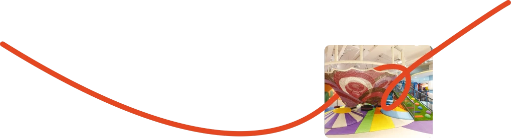 Colorful playground with green structures, a large clock, flowers, and city skyline in the background.