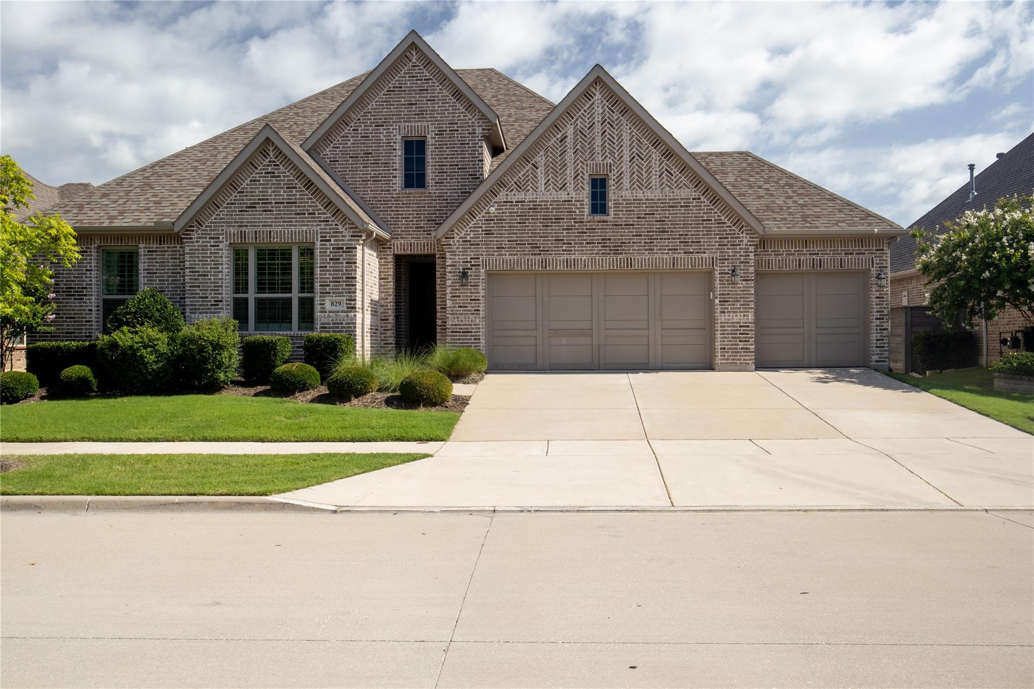 View of front of property with brick siding, a shingled roof, concrete driveway, and a front yard