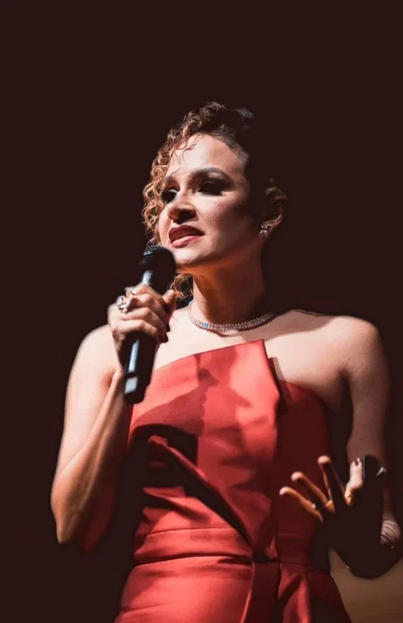 Ítala dos Anjos no palco, de vestido vermelho, falando ao microfone